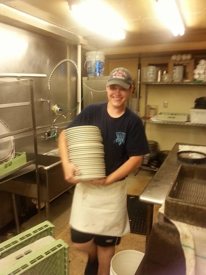 Smiling kitchen worker holding a stack of plates in a restaurant kitchen