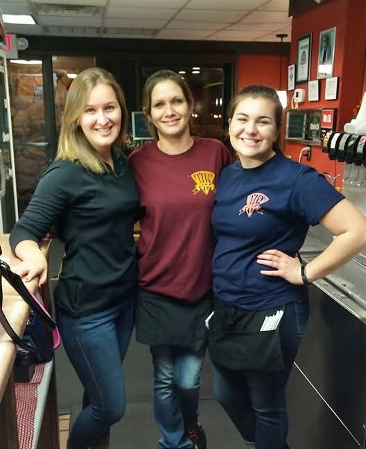 Three smiling people in maroon and black uniforms posing indoors near a counter.