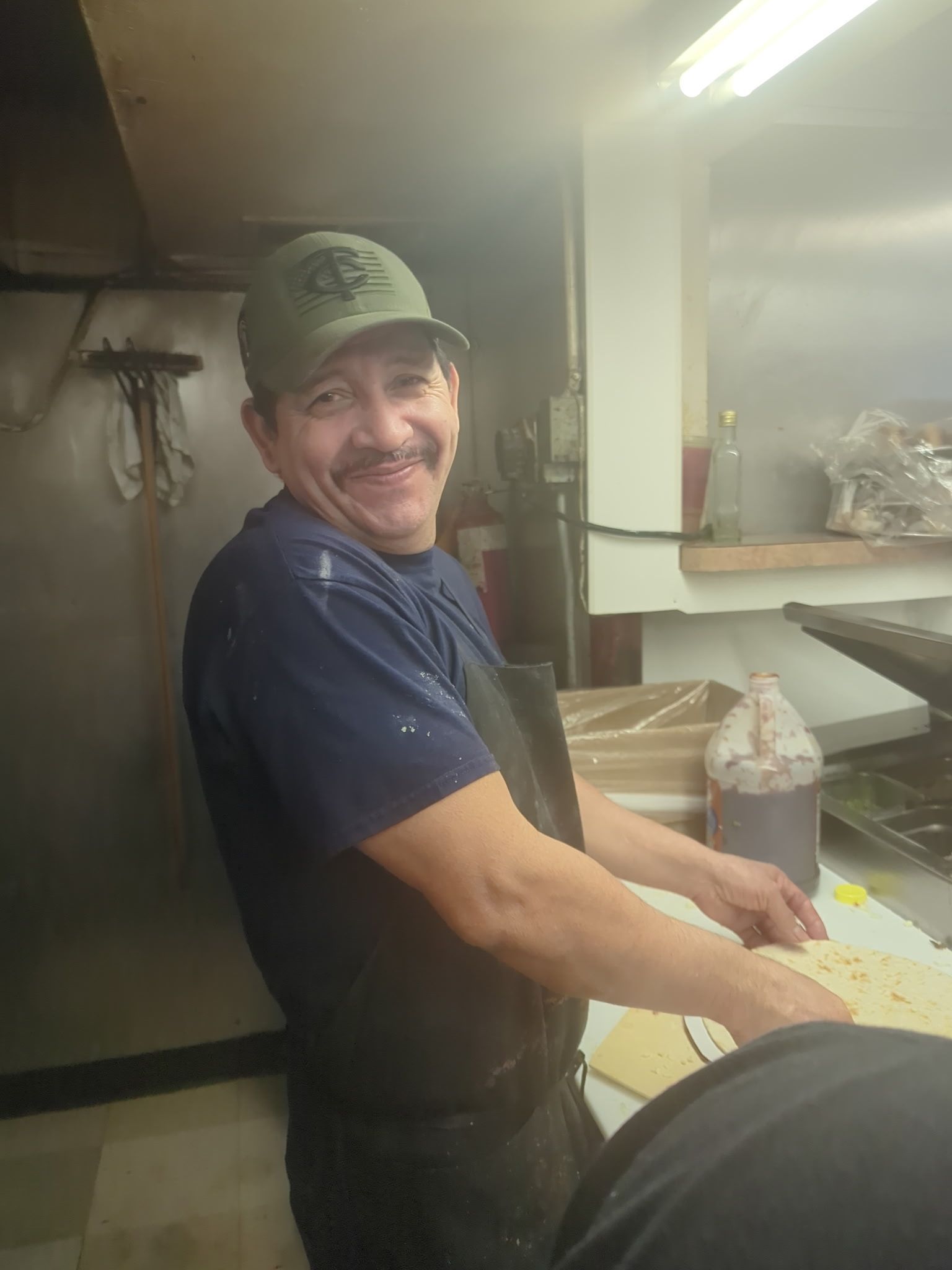 Smiling worker in a cap and apron preparing food at a kitchen counter.