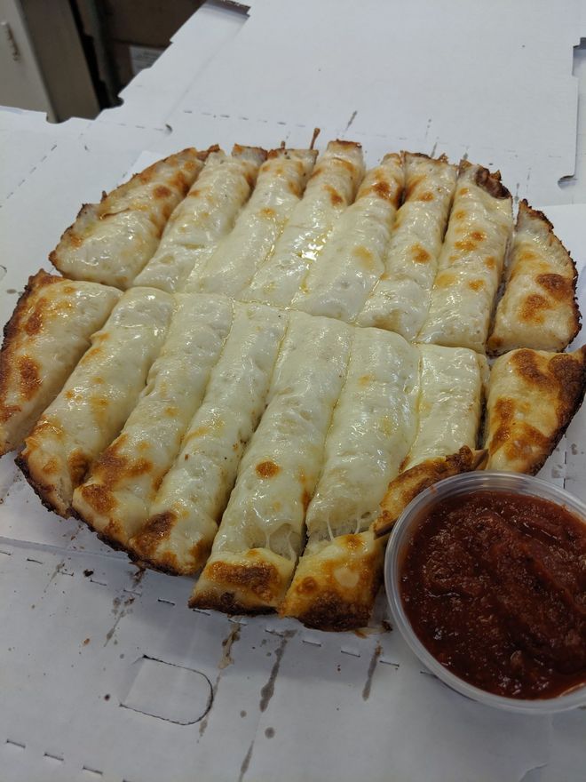 Cheesy baked dish cut into strips, served with a small cup of red sauce on a white tray.
