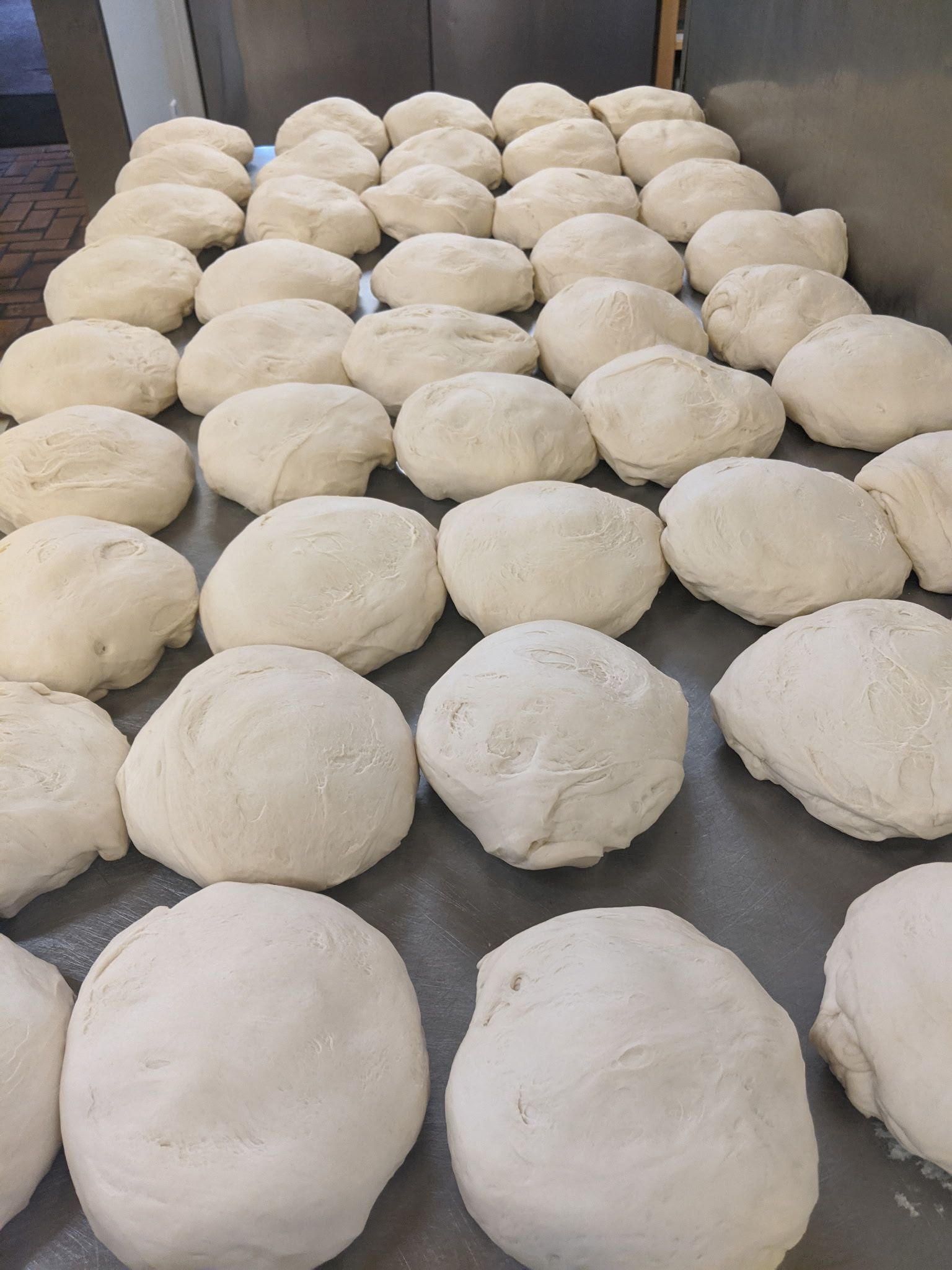Rows of risen dough balls on metal trays in a bakery prep area