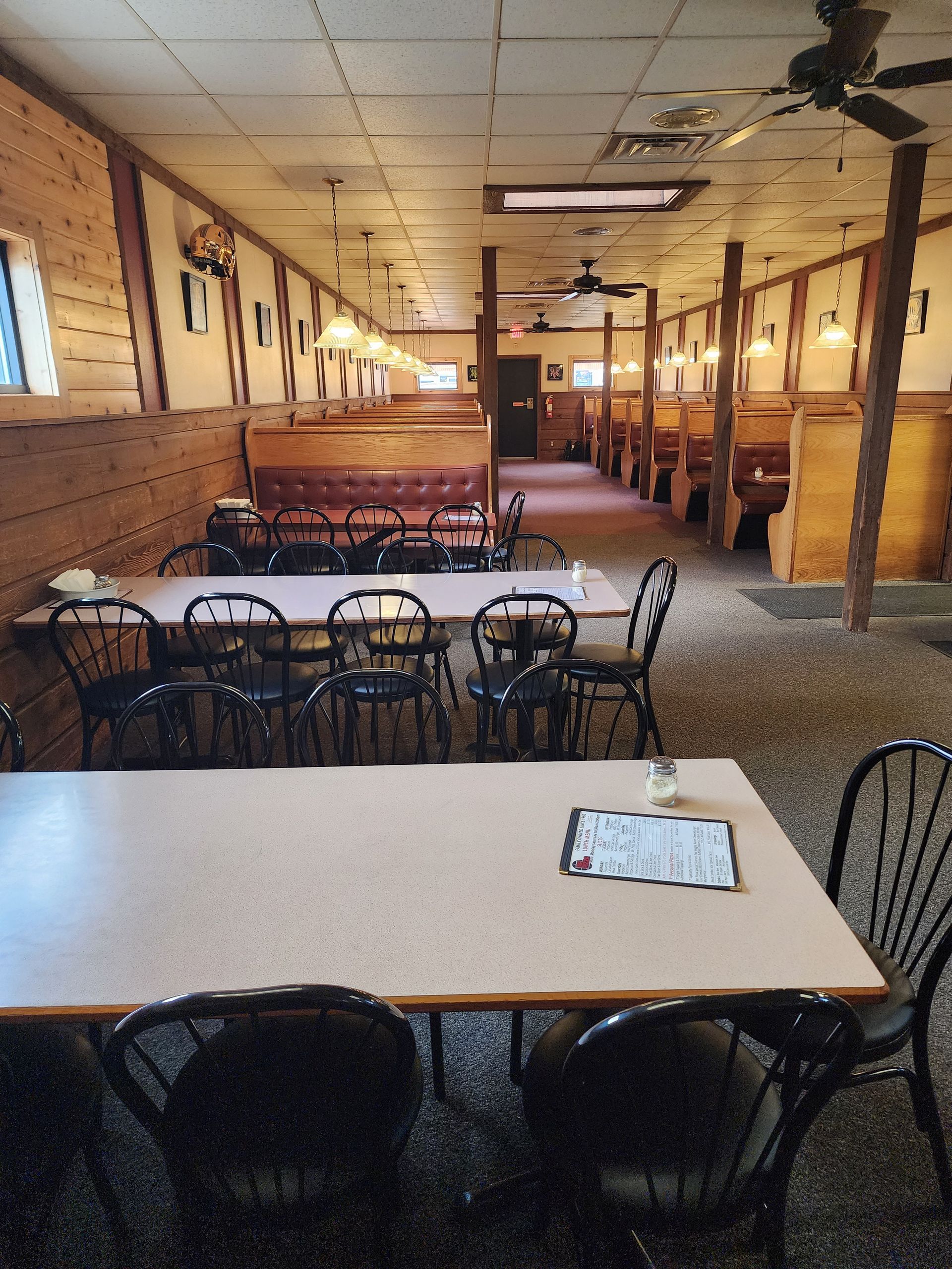 Empty restaurant dining area with tables, black chairs, brick walls, and warm pendant lighting.