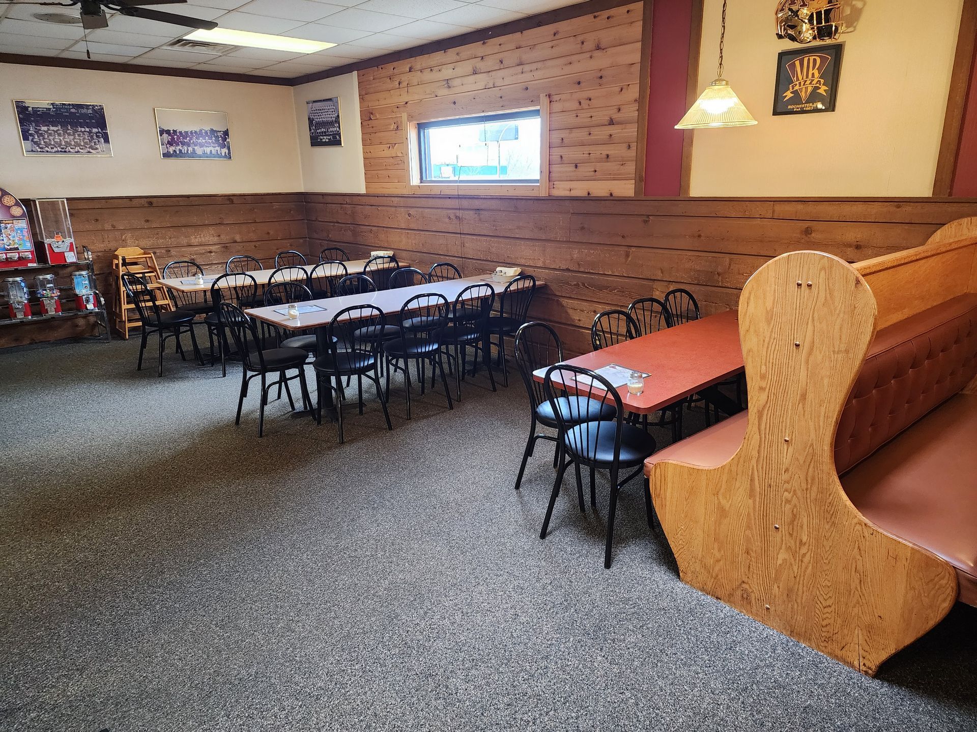 Empty restaurant dining area with checkered tables, black chairs, and red booth seating along wood-paneled walls
