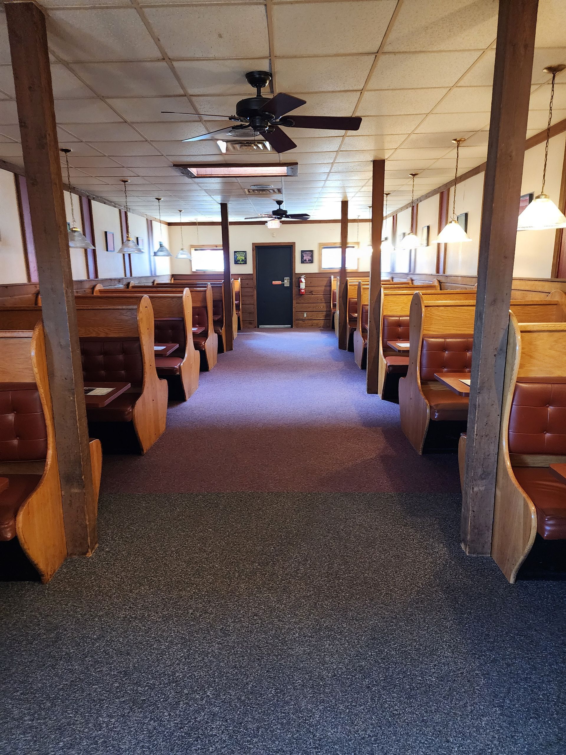 Empty diner interior with wooden booths, ceiling fans, and carpeted aisle leading to the back door