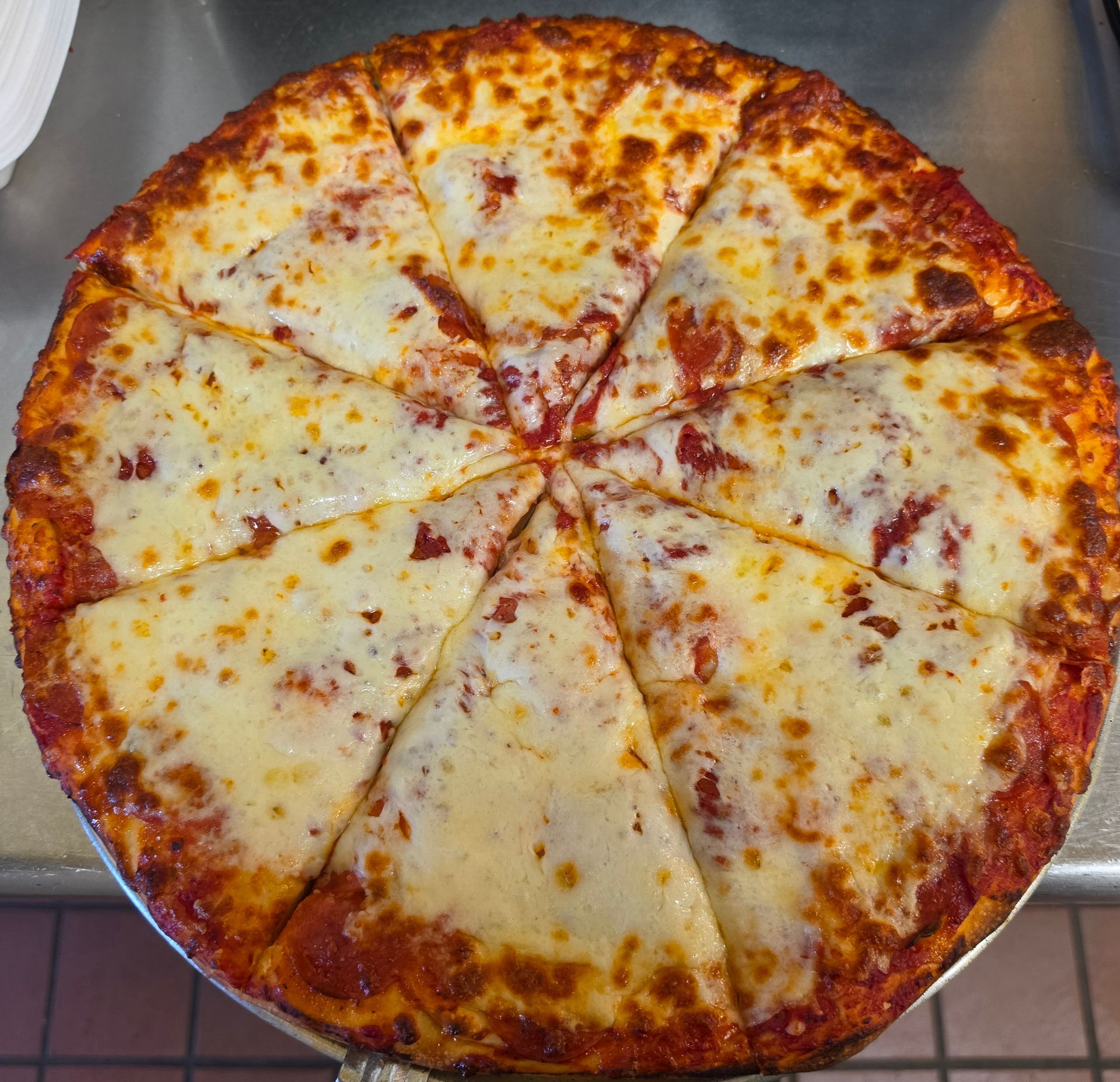 Round cheese pizza on a tray, cut into slices, with a browned crust and melted cheese.
