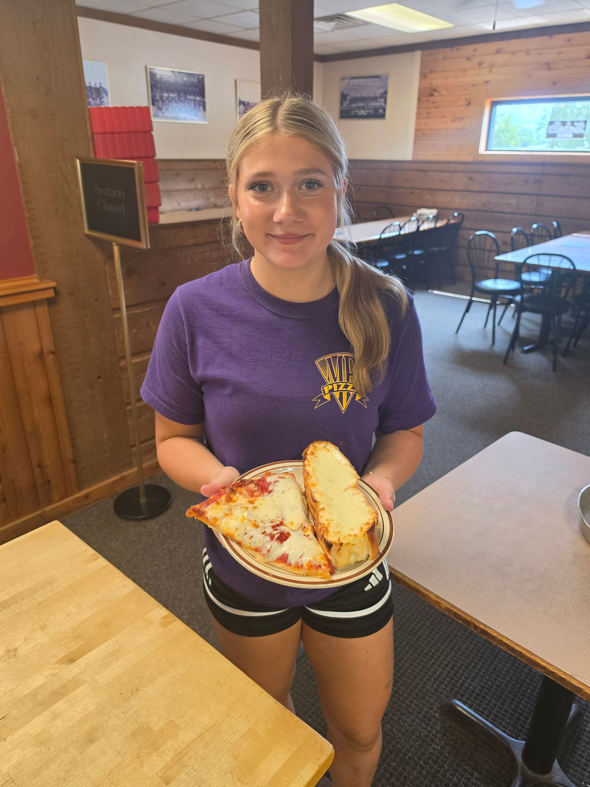 Girl in a purple shirt holding a plate of pizza inside a restaurant