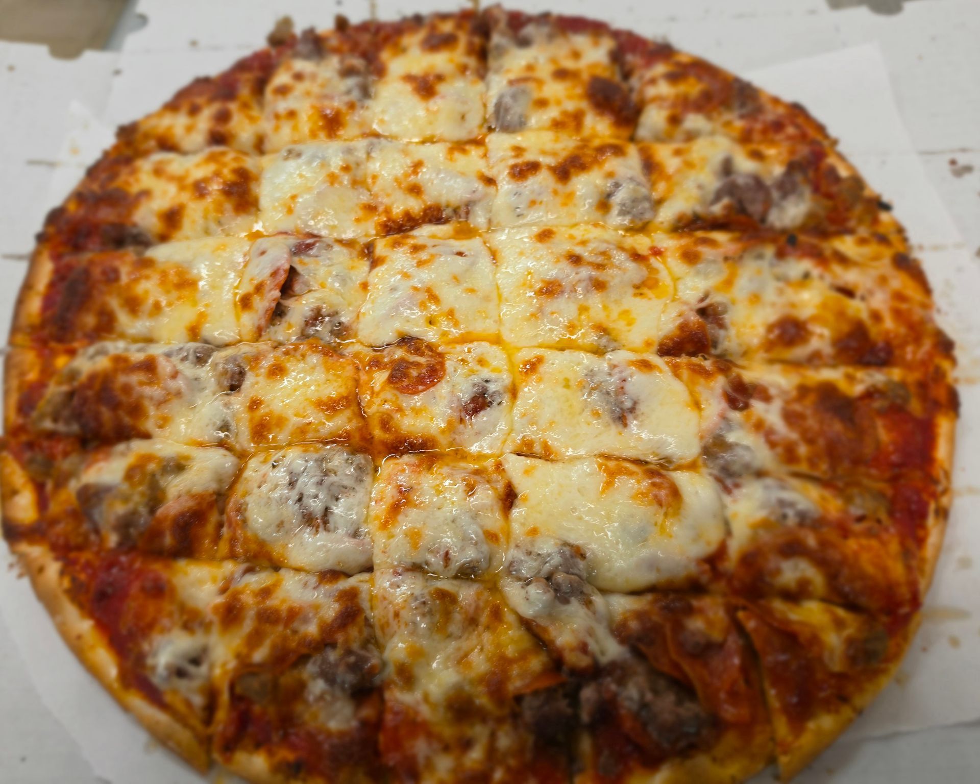 Cheese pizza with browned sausage on a white cardboard box lid