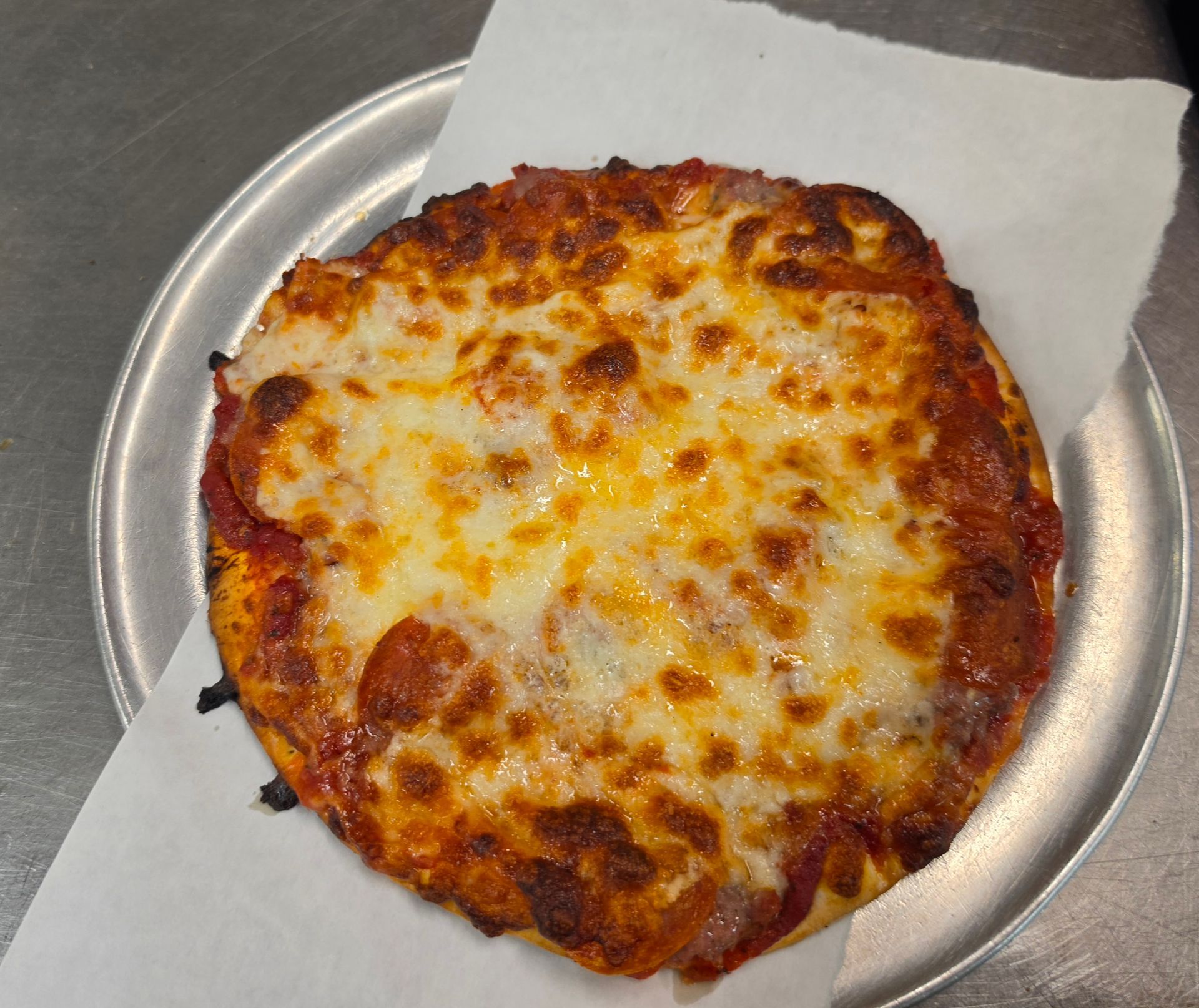 Cheesy personal pizza on a metal tray, with a napkin underneath.