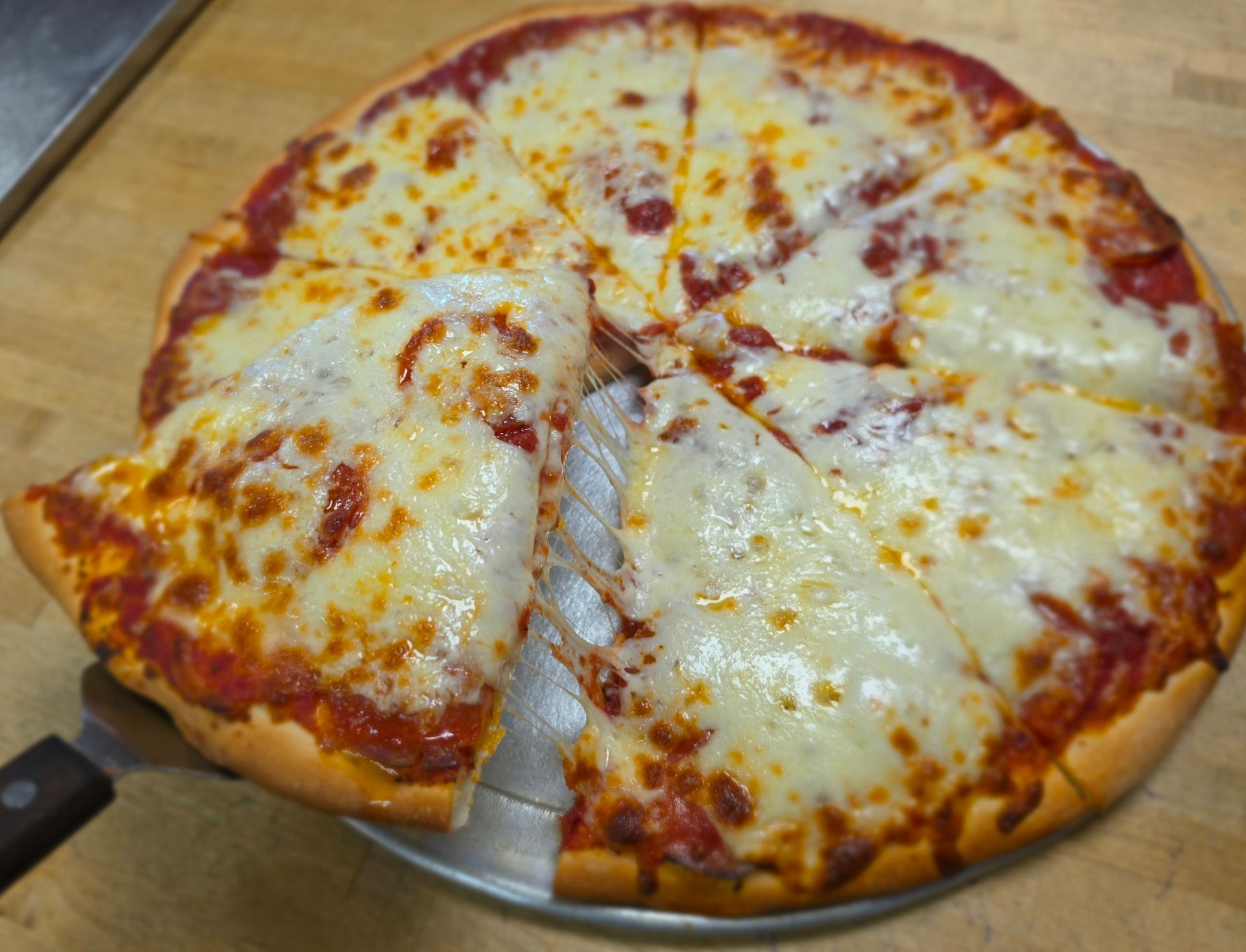 Cheese pizza with a slice being lifted on a wooden cutting board