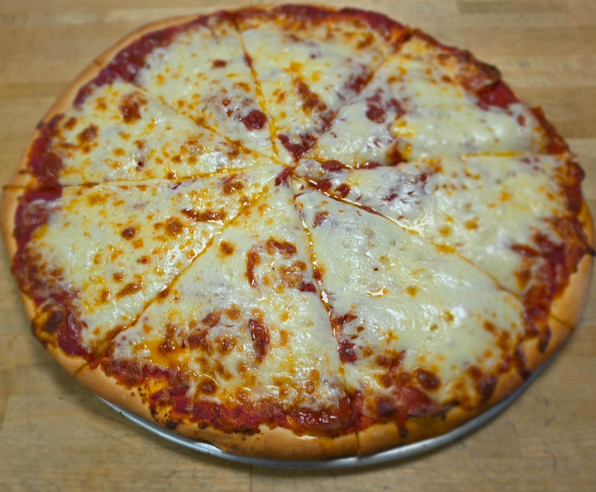 Cheese pizza on a pan, sliced into eight pieces on a wooden surface