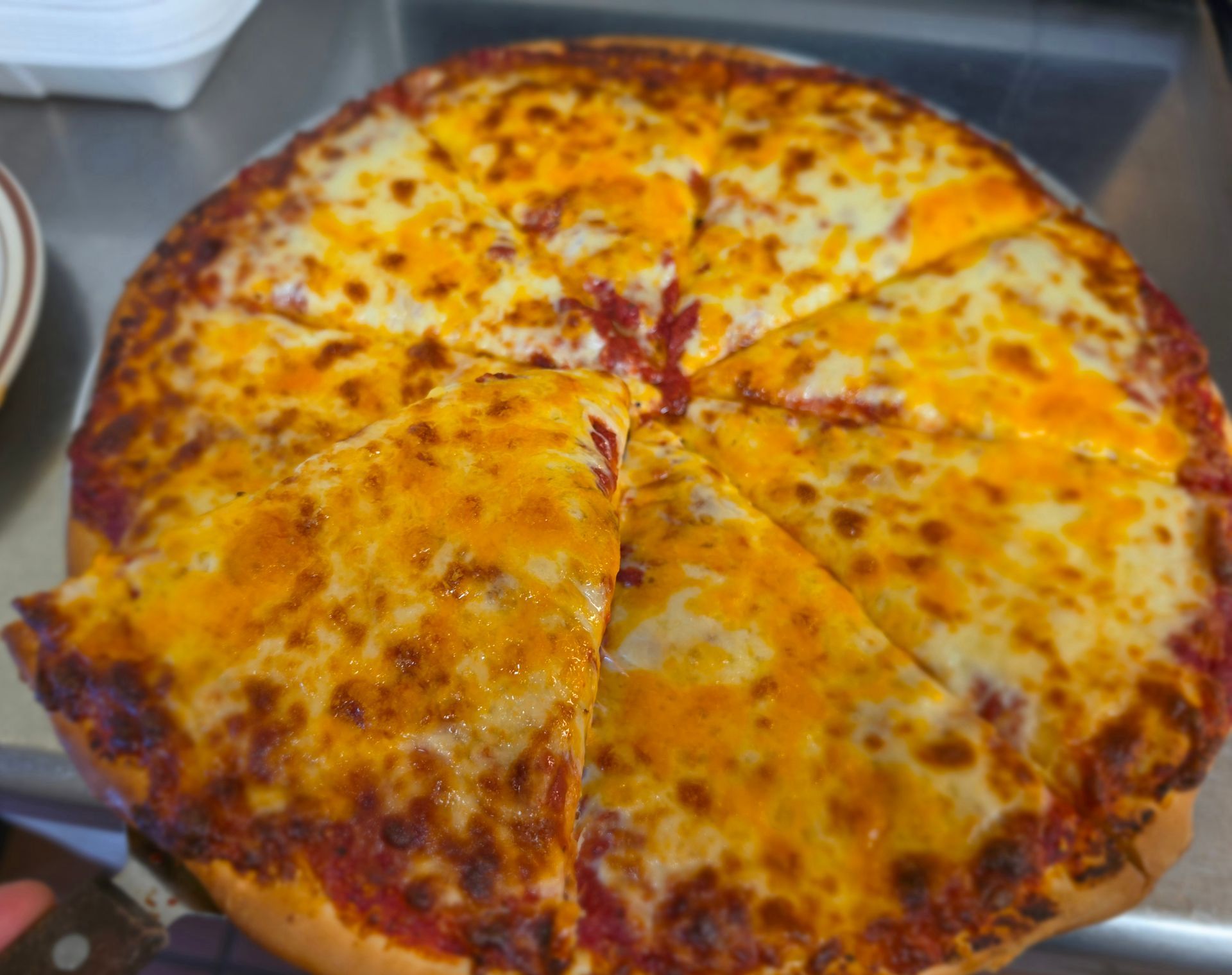 Large cheese pizza in a metal tray, sliced into pieces with browned crust and melted toppings.
