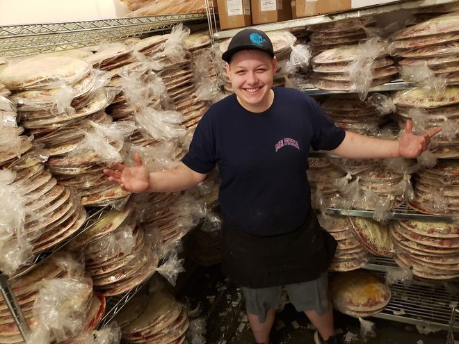 Person smiling with arms outstretched beside stacks of wrapped trays in a storage area