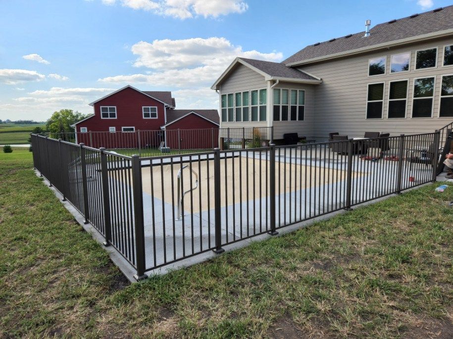 A fence surrounds a swimming pool in front of a house.