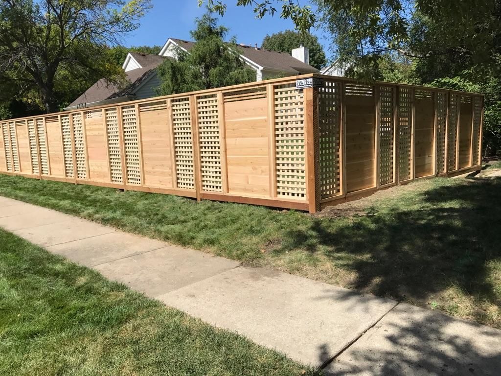 A wooden fence is sitting next to a sidewalk in front of a house.