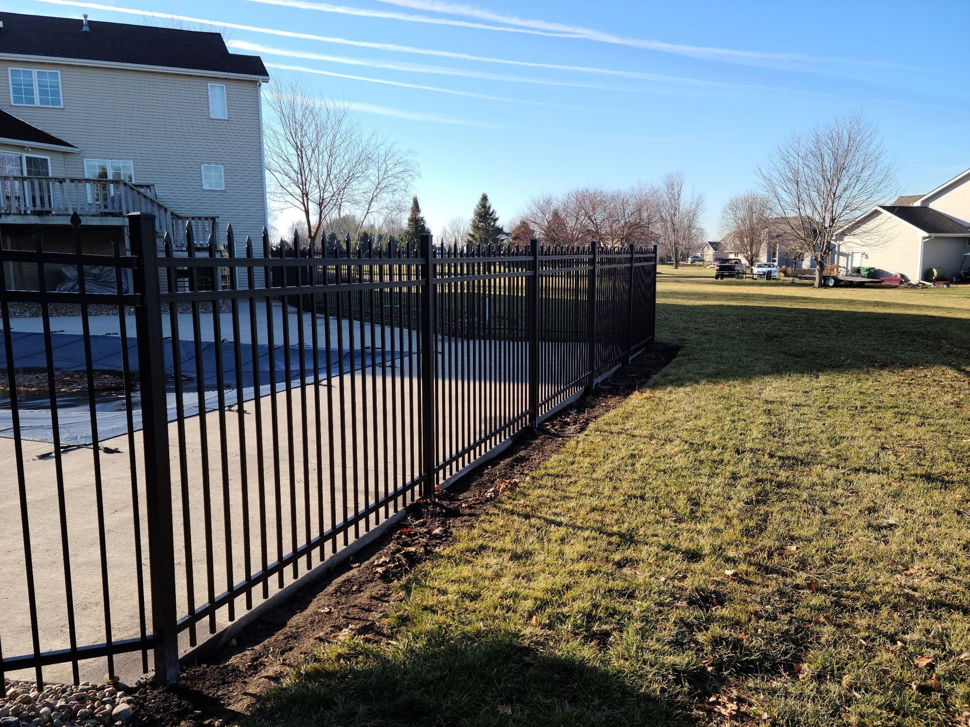 A wrought iron fence surrounds a grassy yard in front of a house