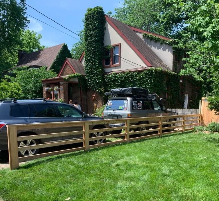 A car is parked in front of a house behind a wooden fence