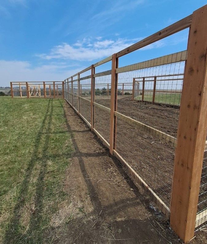 A wooden fence surrounds a grassy field on a sunny day.