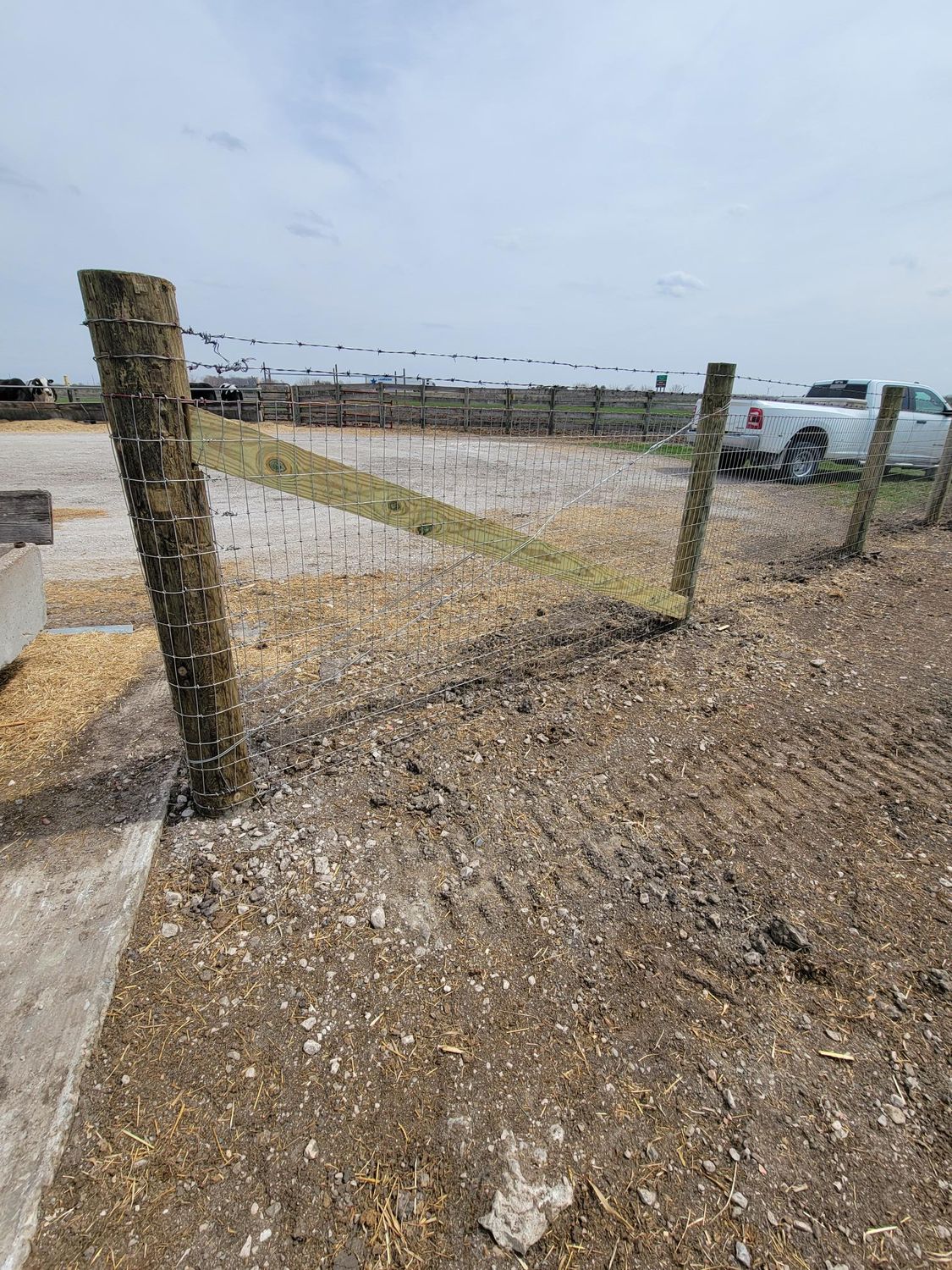 A white truck is parked next to a fence in a dirt field.