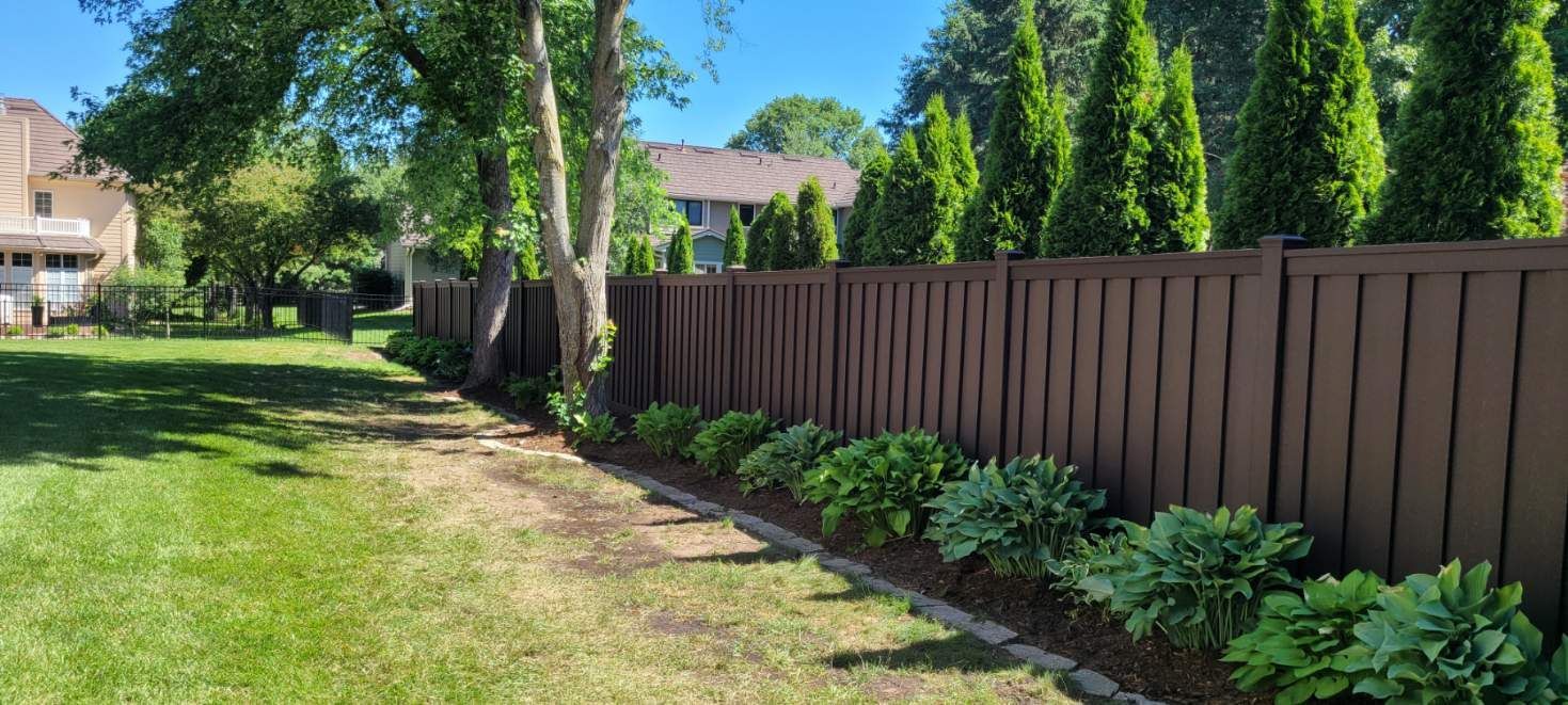 A wooden fence surrounds a lush green yard with trees and bushes.