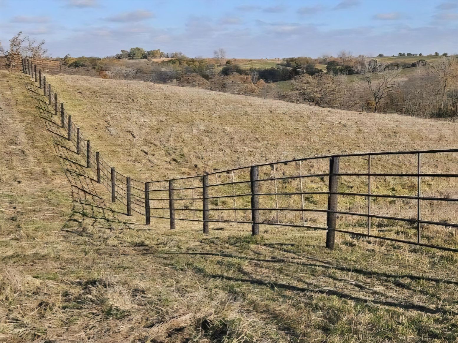 Fence along a grassy hill, under a blue sky, in a rural landscape.