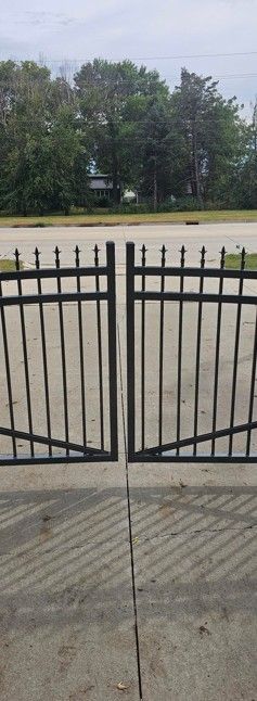 Black metal gate on concrete, with trees and sky in the background.