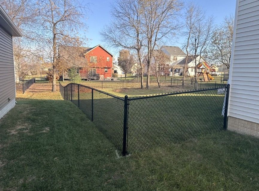 Black chain-link fence in backyard with houses in the background on a sunny day.