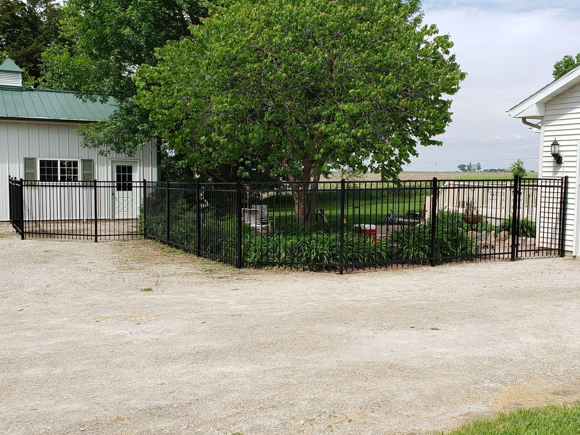 A black fence surrounds a gravel driveway in front of a white house.