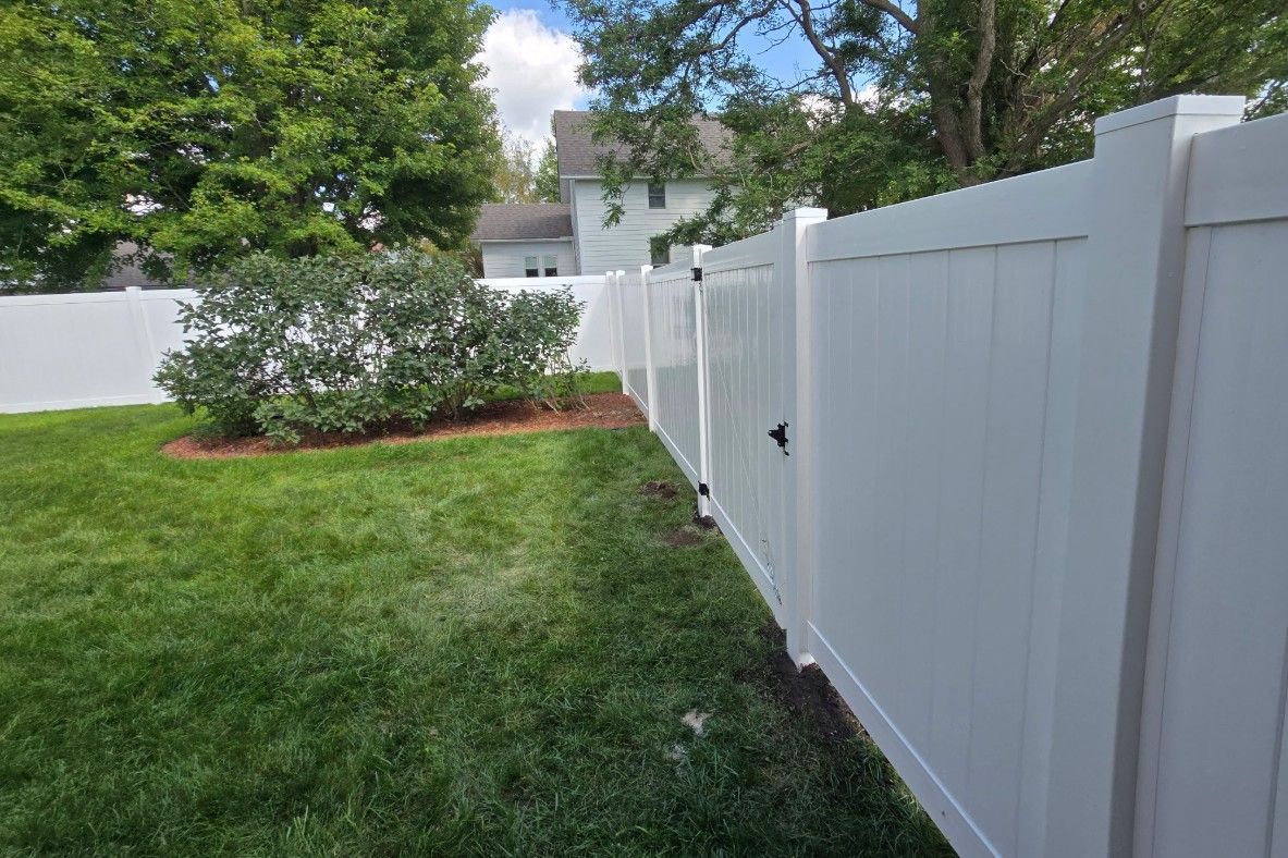 White vinyl fence enclosing a green lawn and shrubbery.  A house is visible in the background.