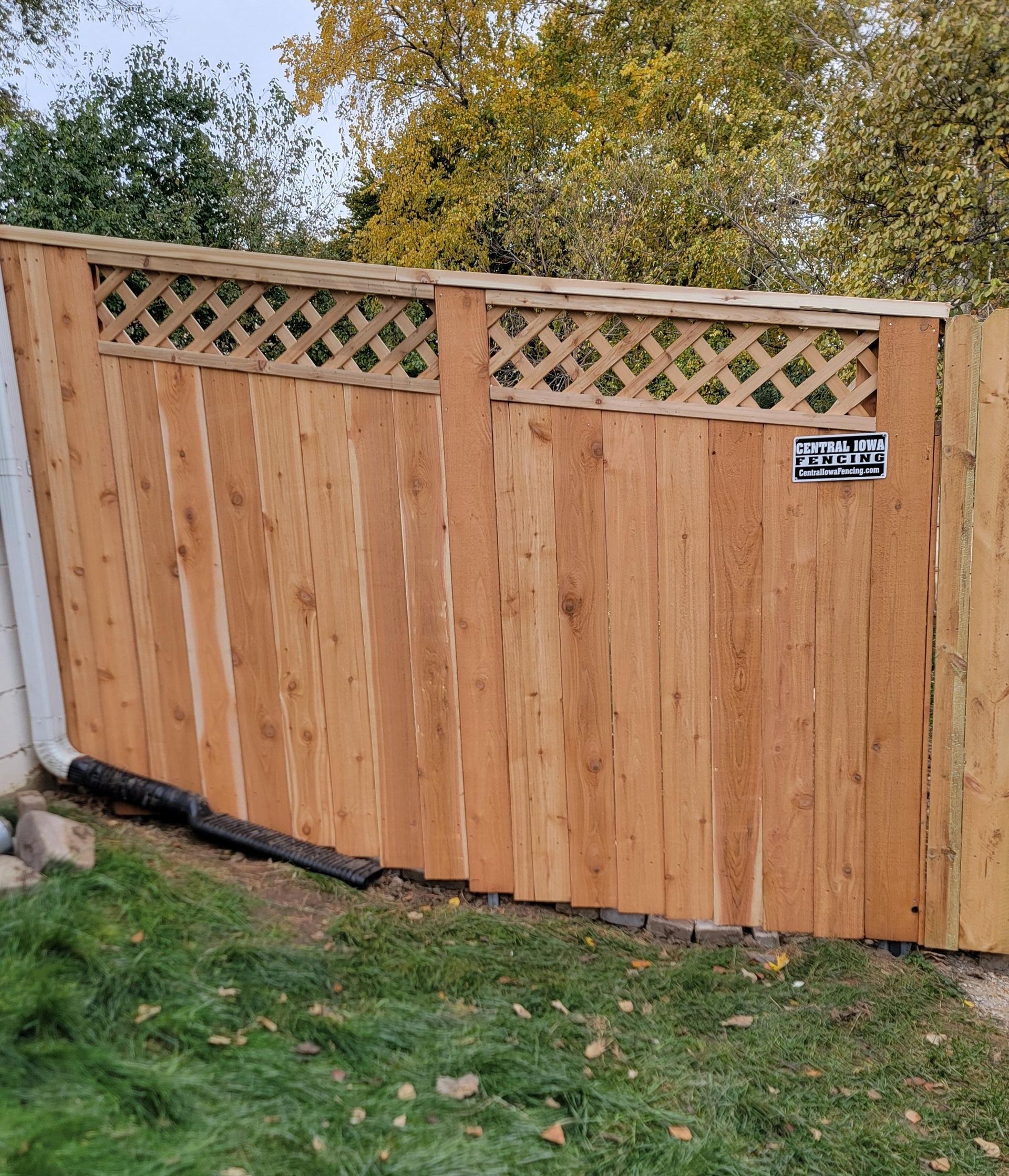 Wooden fence with lattice top in a yard with green grass and trees.
