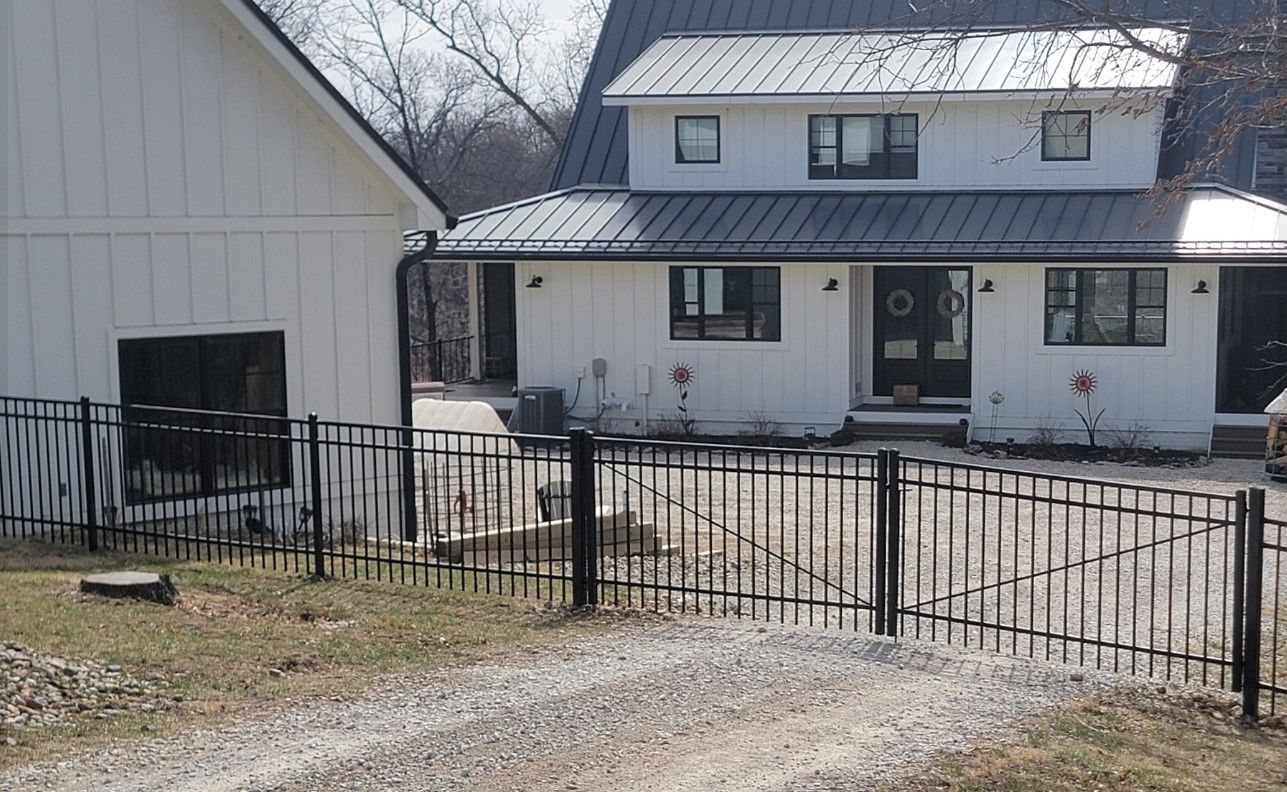 A white house with a black roof and a black fence in front of it.
