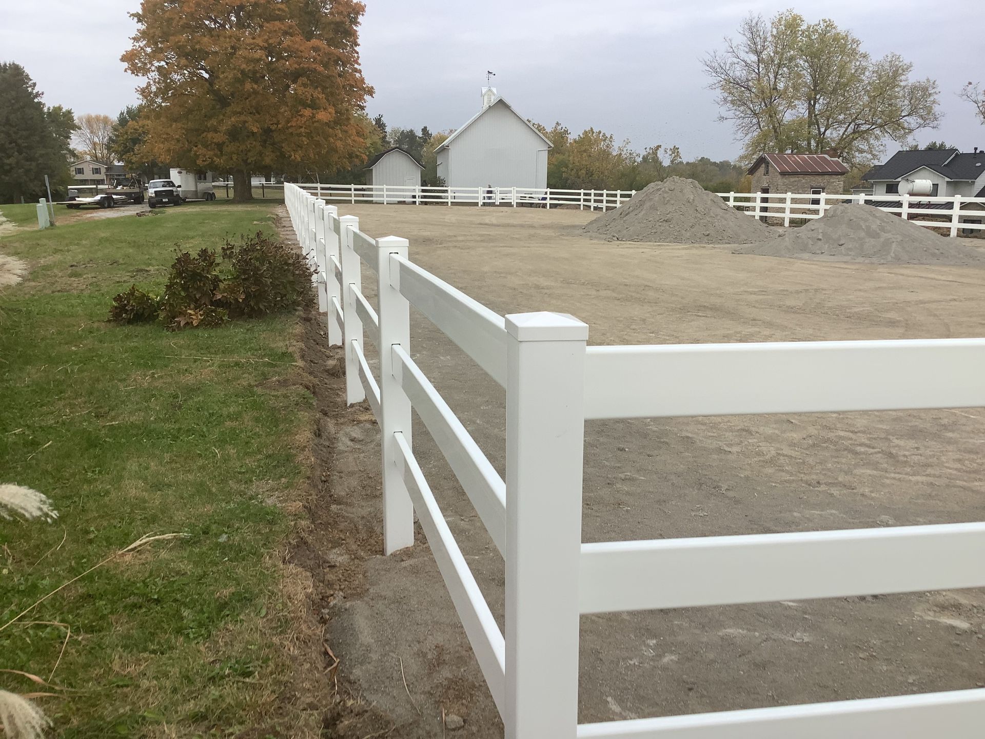 A white fence surrounds a dirt field with a small white building in the background