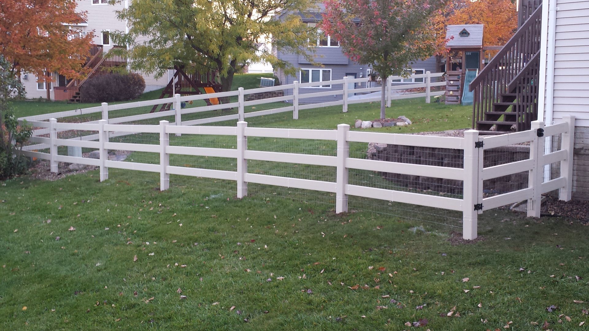 A white fence surrounds a lush green yard in front of a house.