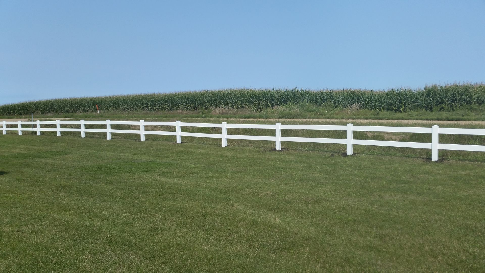 A white fence surrounds a lush green yard in front of a house.