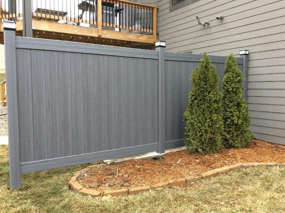 A gray fence is in the backyard of a house.