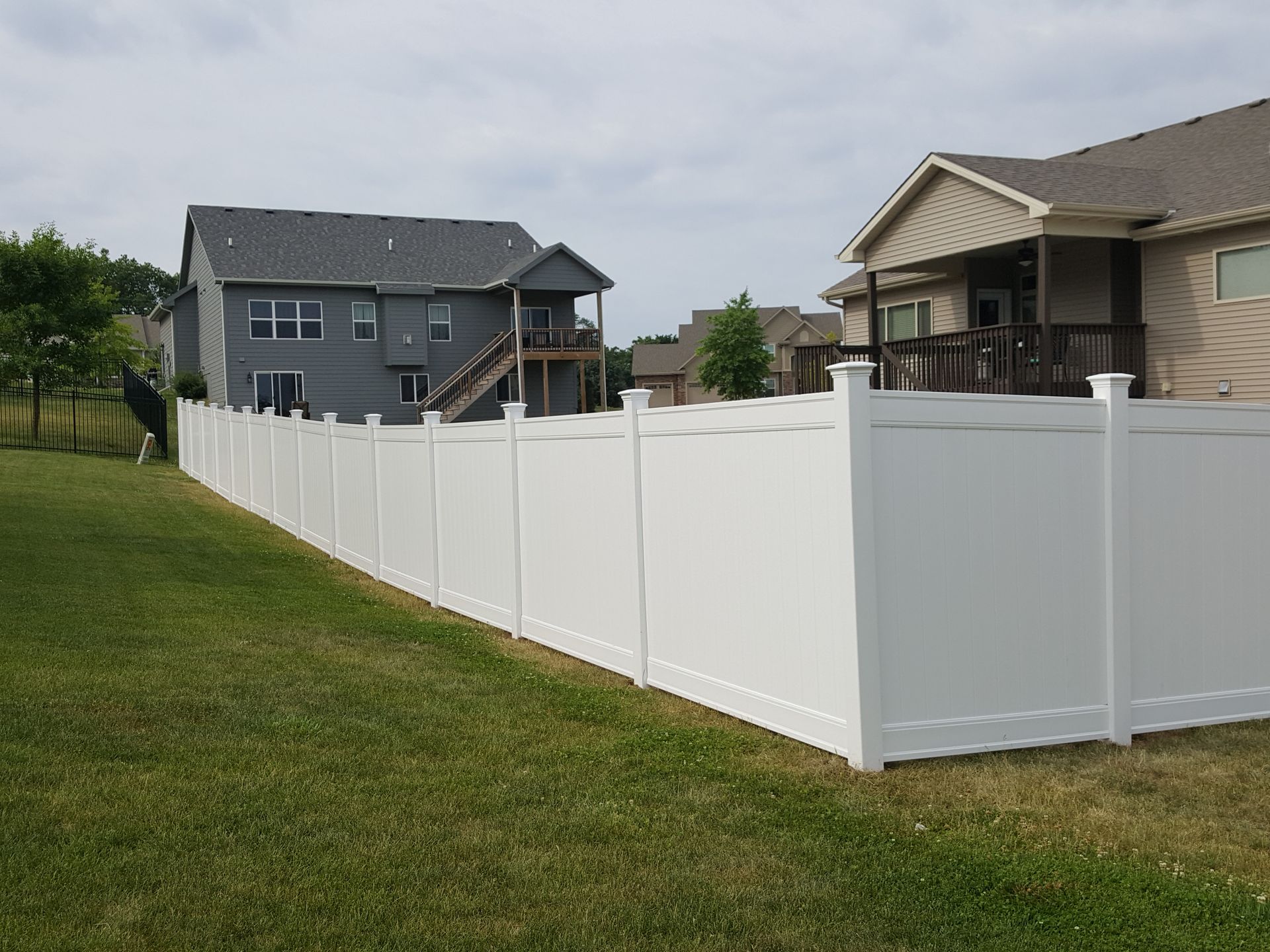 A white fence surrounds a lush green yard in front of a house.