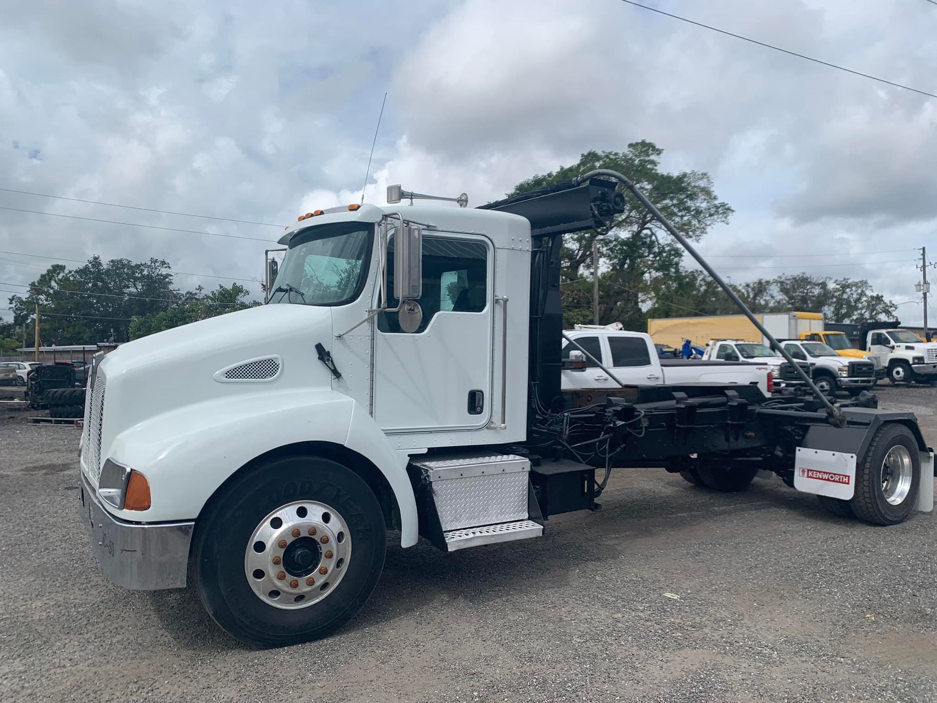 White roll-off truck parked outdoors on a gravel lot under a cloudy sky.