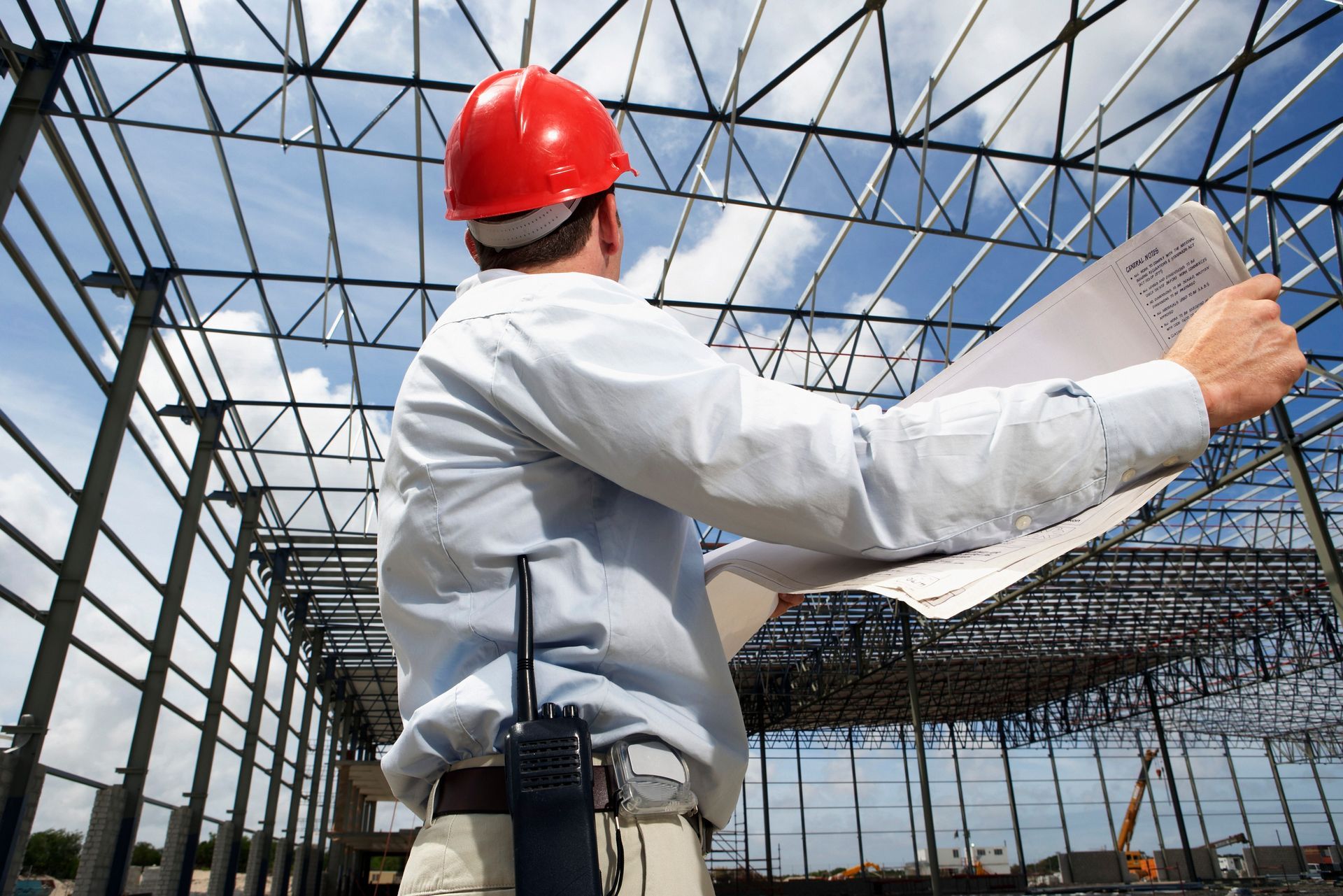 A man wearing a hard hat is looking at a blueprint in a building under construction.