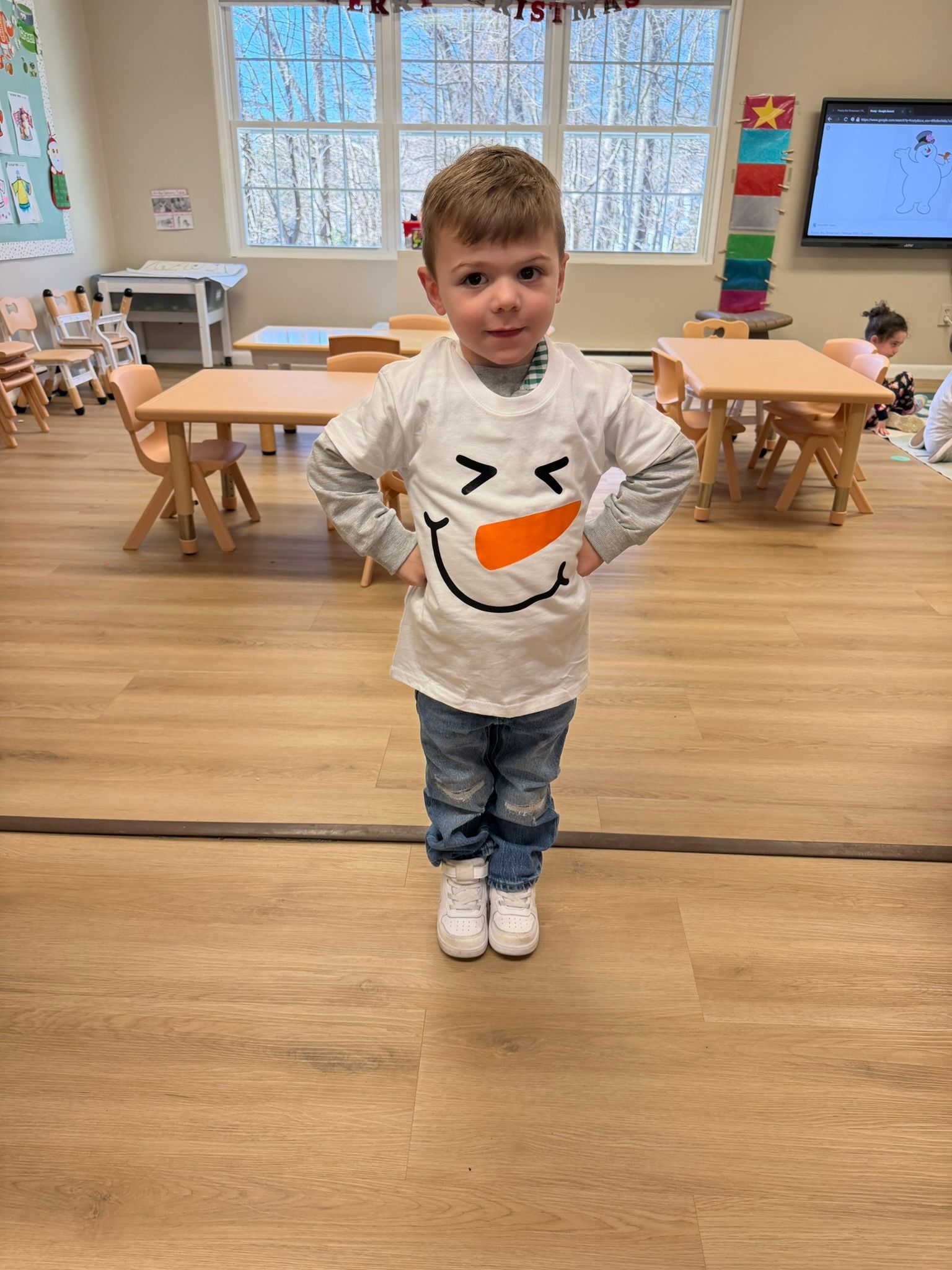 Boy in snowman shirt with hands on hips in classroom.