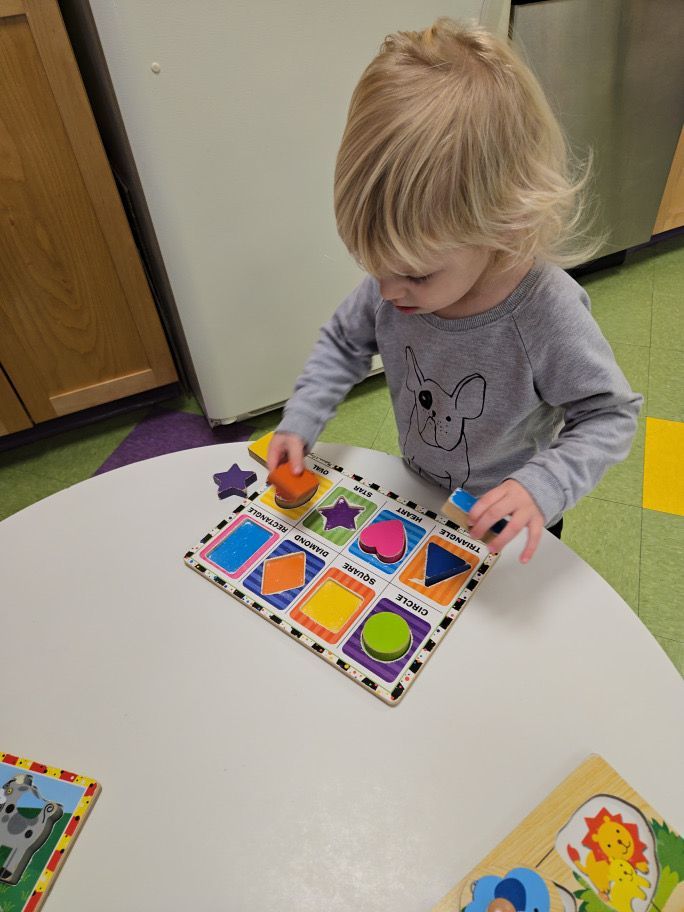 Child playing with a shape puzzle at a table, indoors.