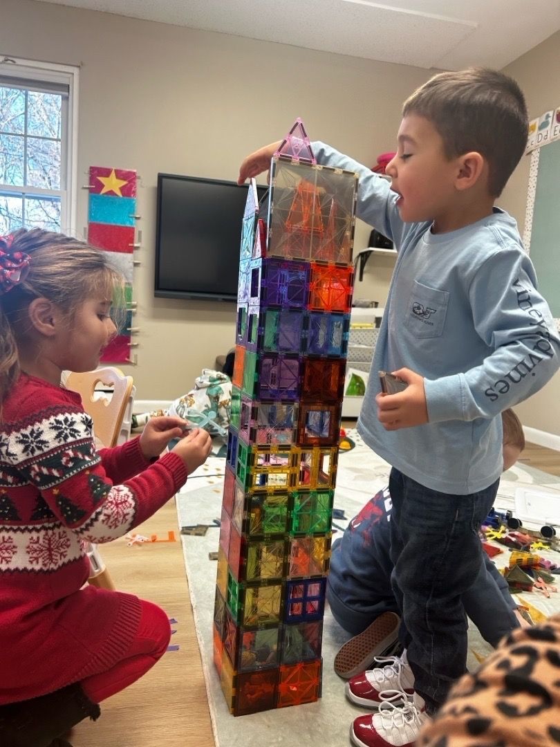 Two children building a tall tower with colorful magnetic tiles inside a room.