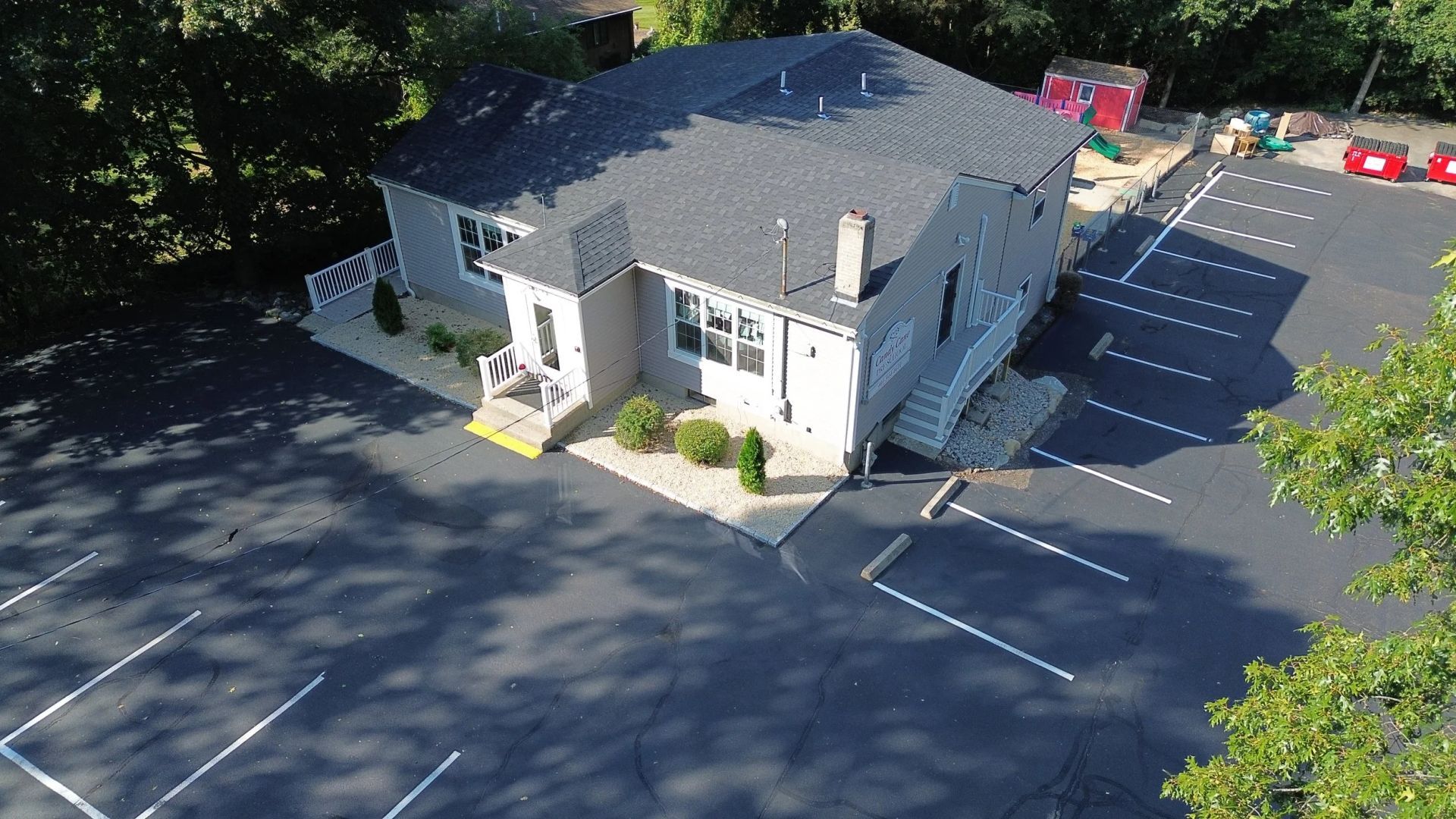Building with parking lot. Light-colored building with dark roof, surrounded by trees and a paved parking lot with white lines.