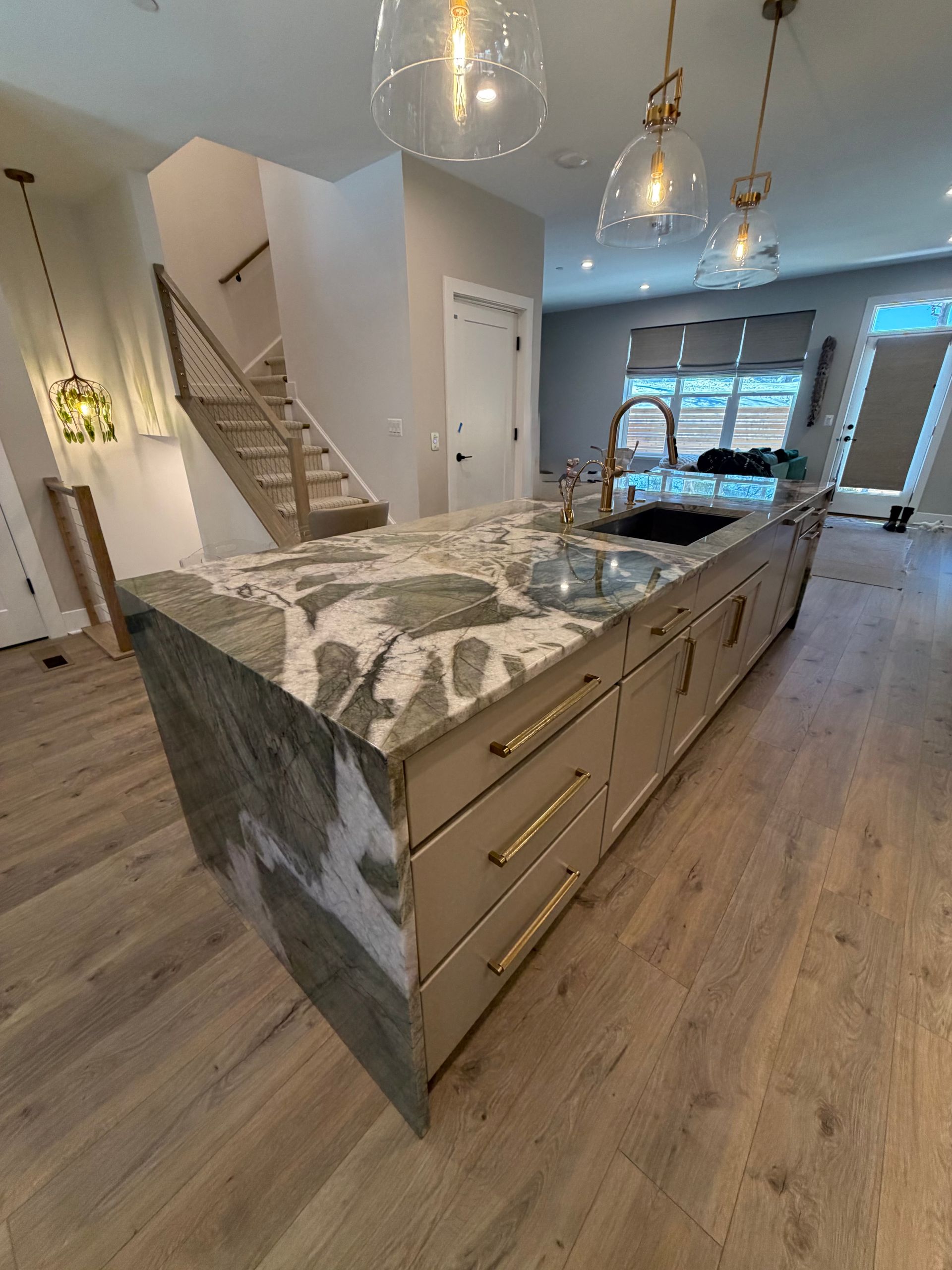 Modern kitchen with large marble island, gold hardware, pendant lights, and open view to dining area and staircase