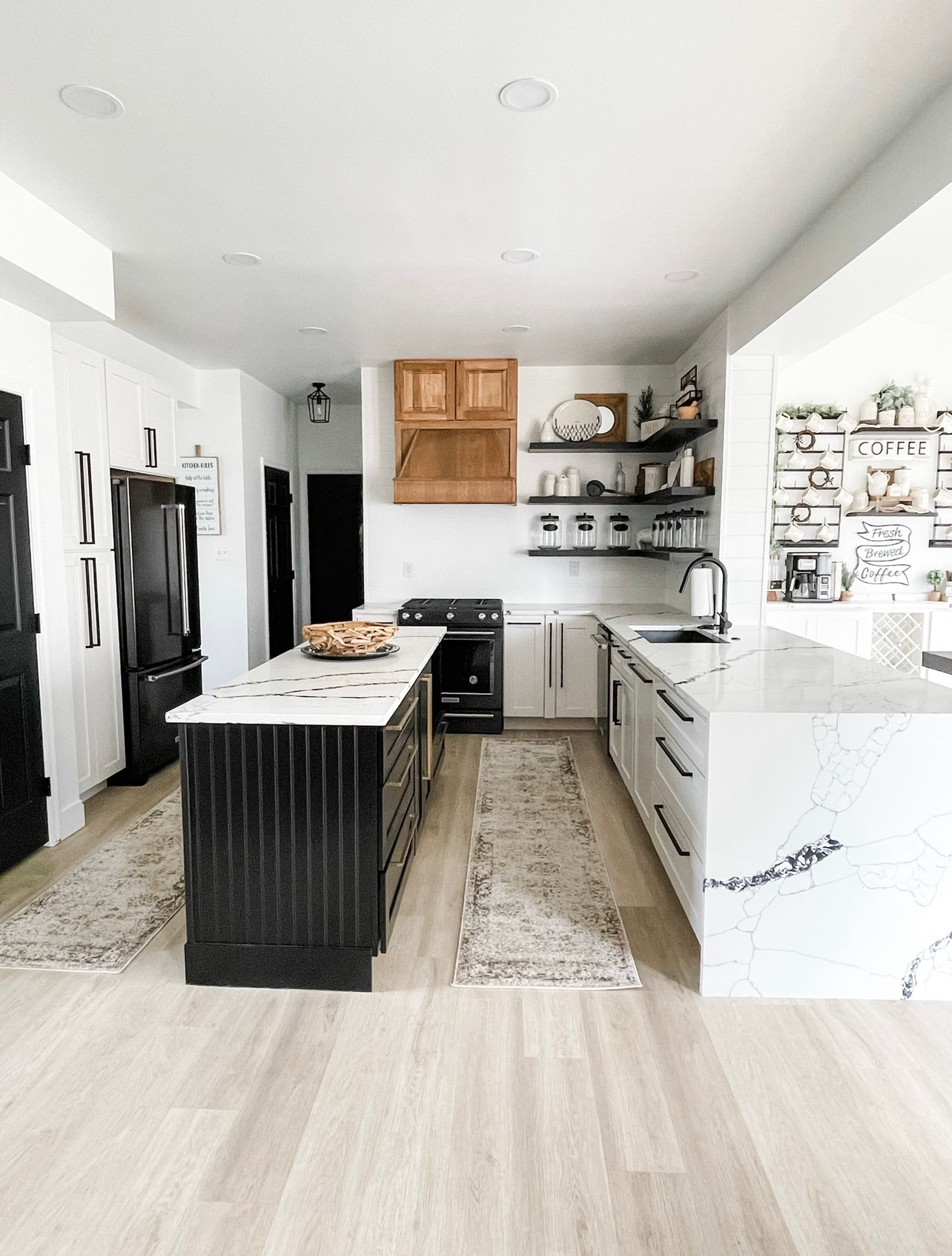 Bright modern kitchen with white cabinets, black island, open shelves, and marble countertops