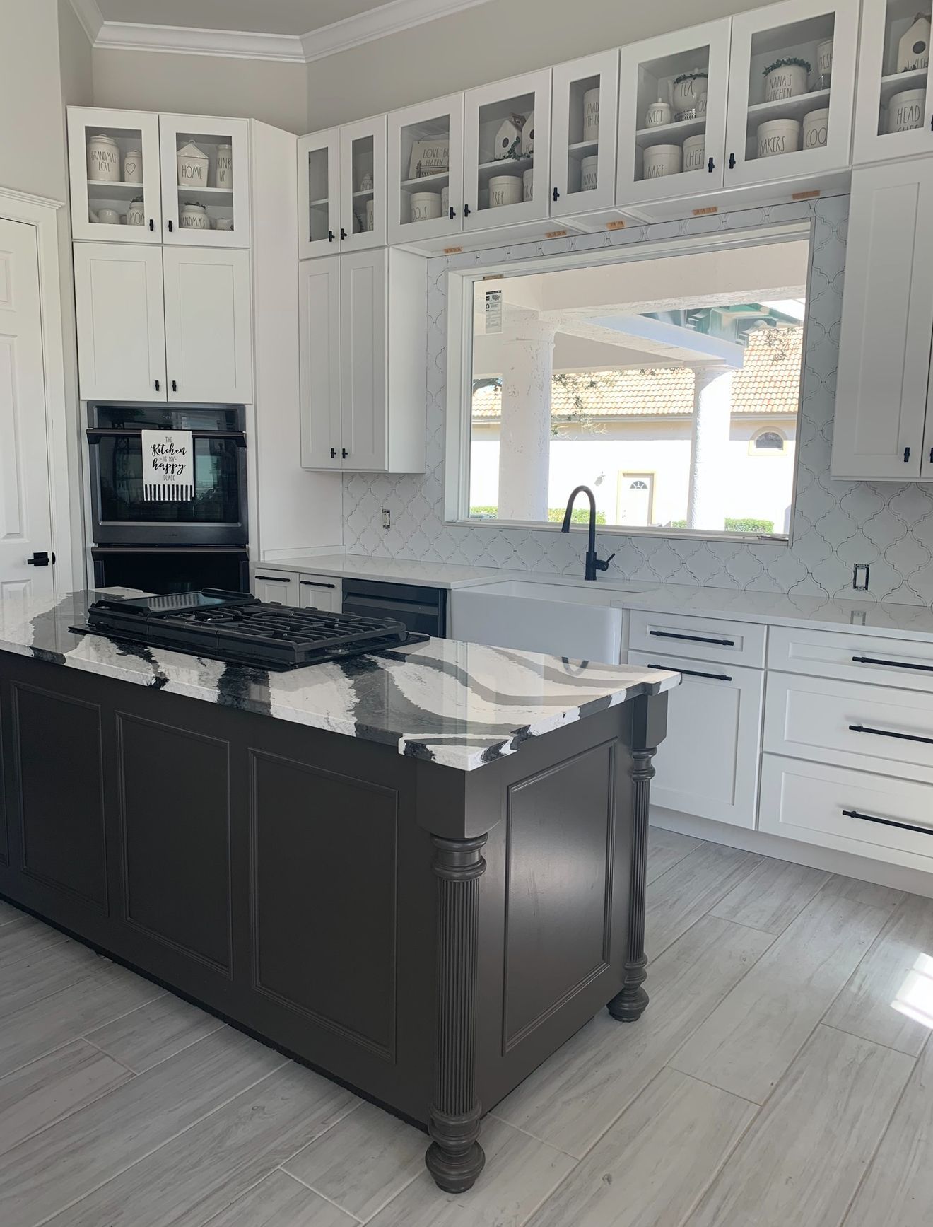 Modern white kitchen with black island, marble countertops, and large window above the sink