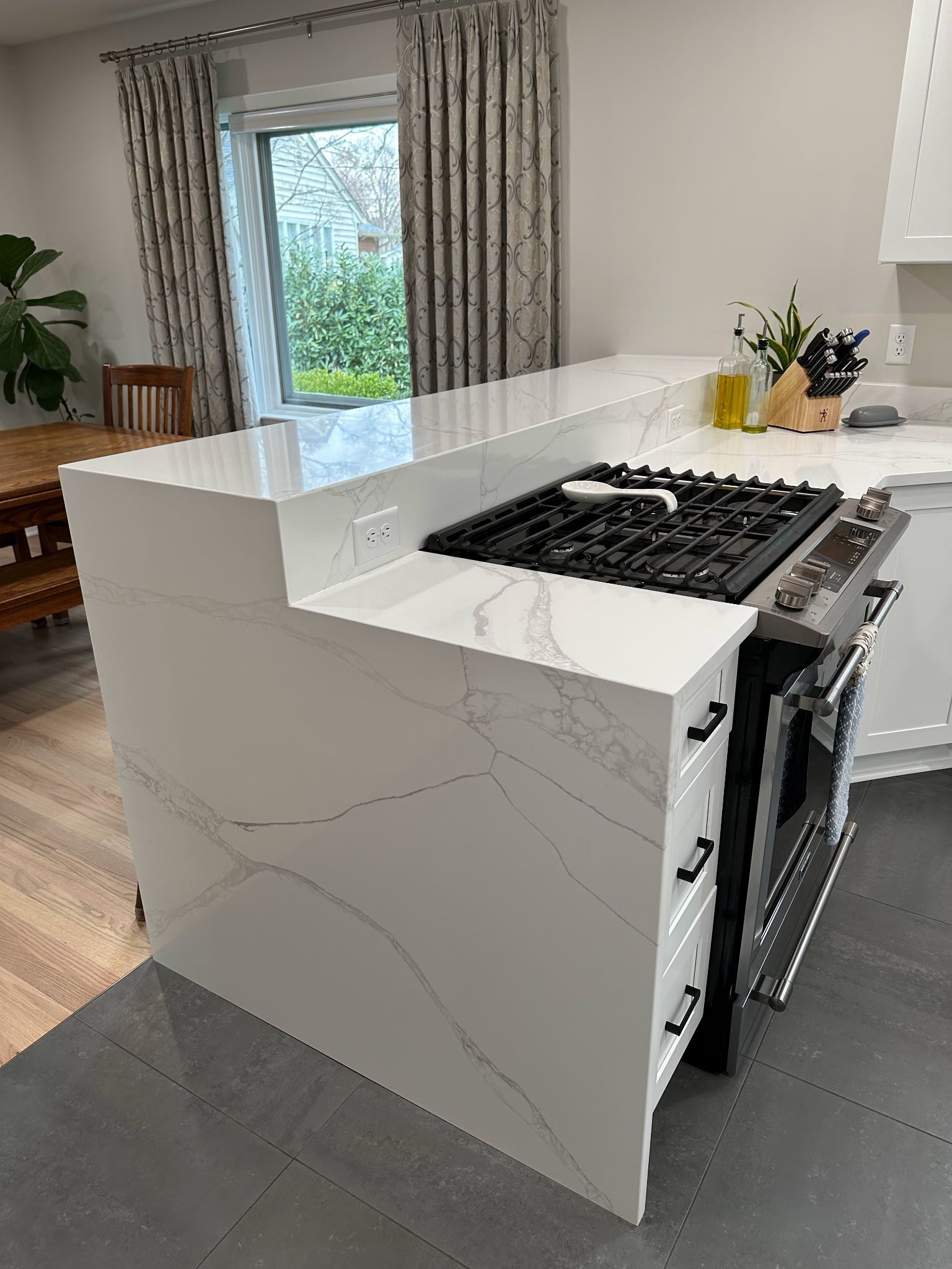 Modern kitchen island with white marble-look panels and a black gas cooktop beside a bright window.