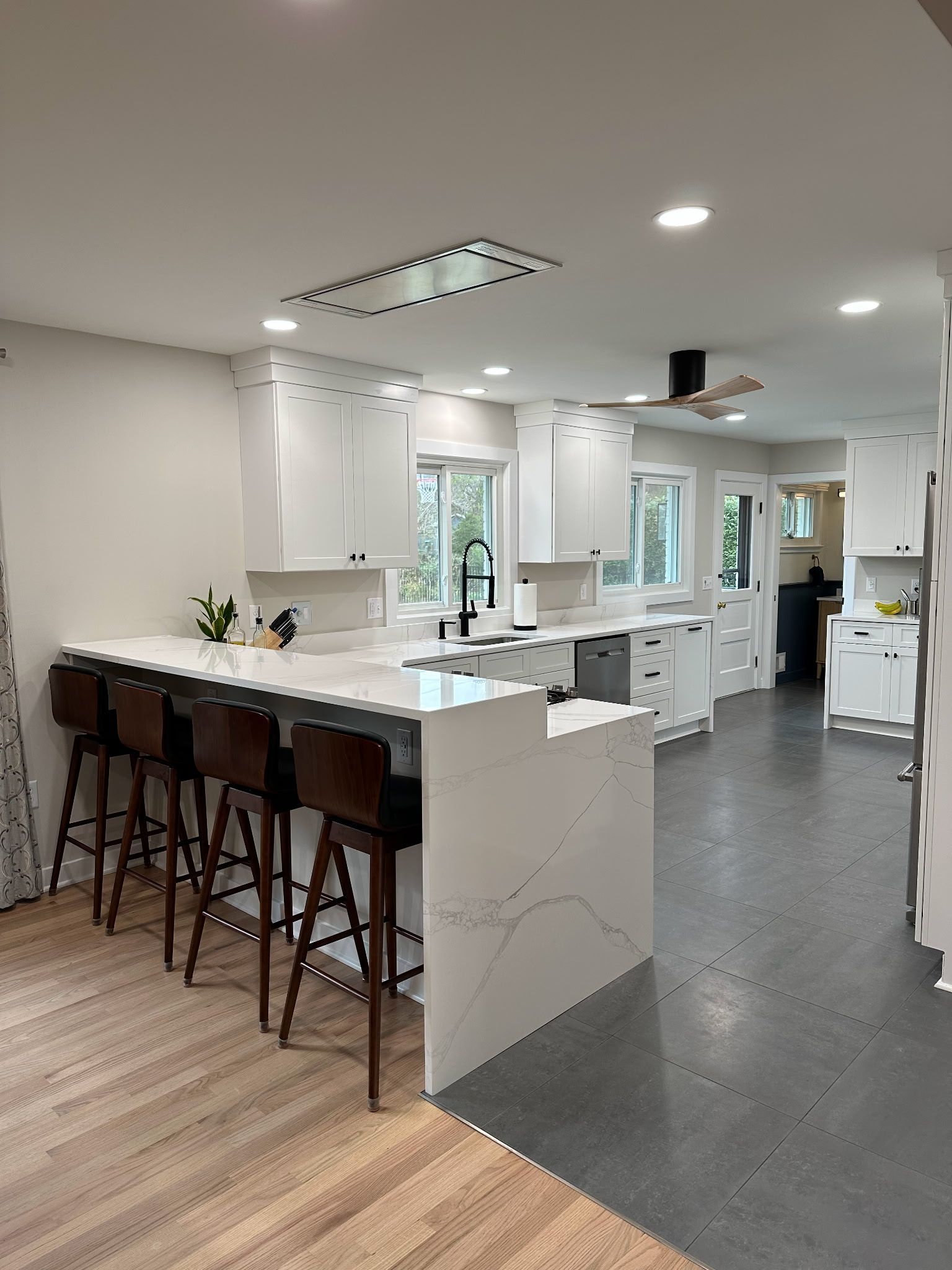 Bright modern kitchen with white island, black stools, and gray flooring leading to a living area