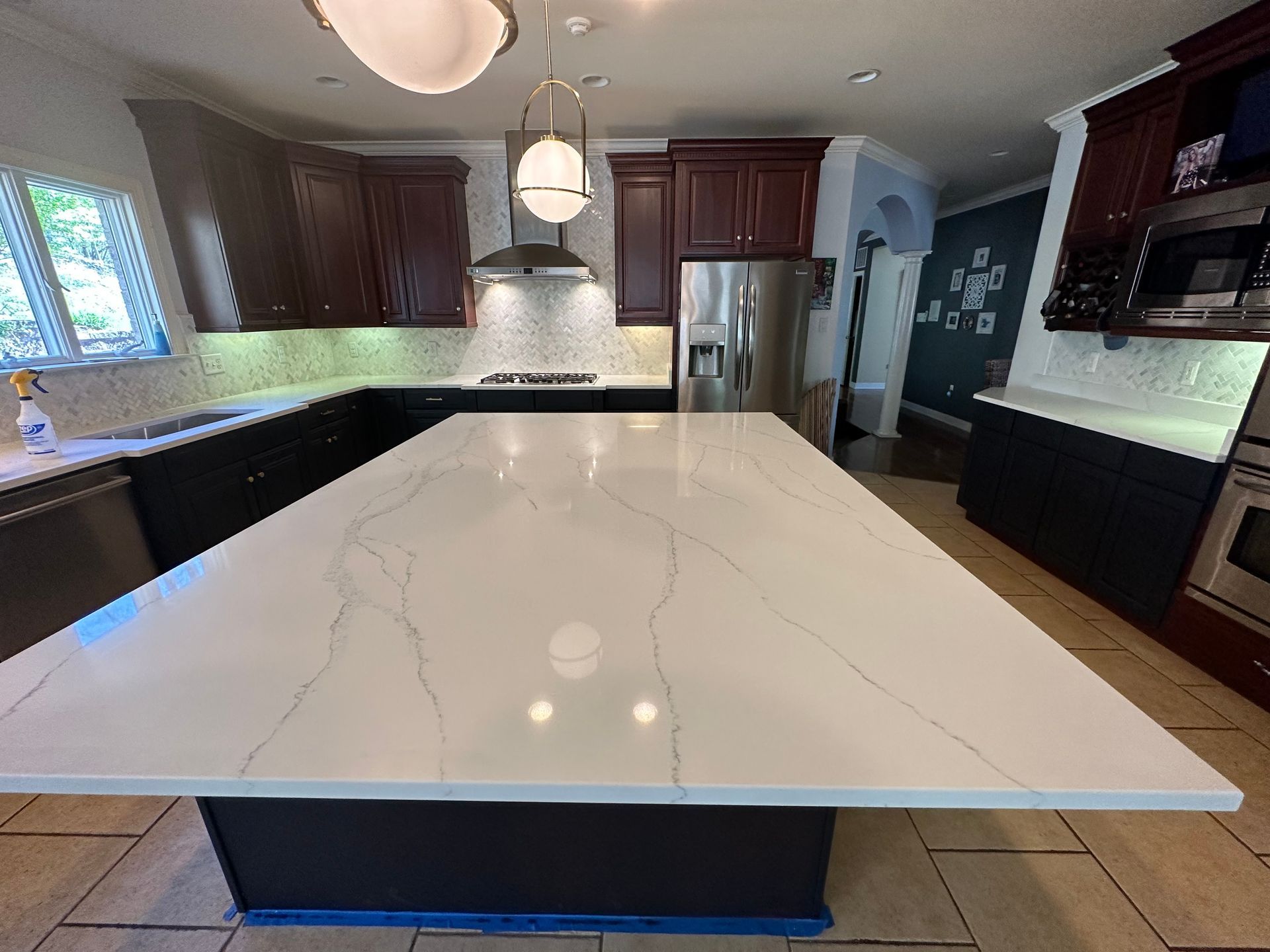 Modern kitchen with white marble island, dark cabinets, pendant lights, and stainless range hood