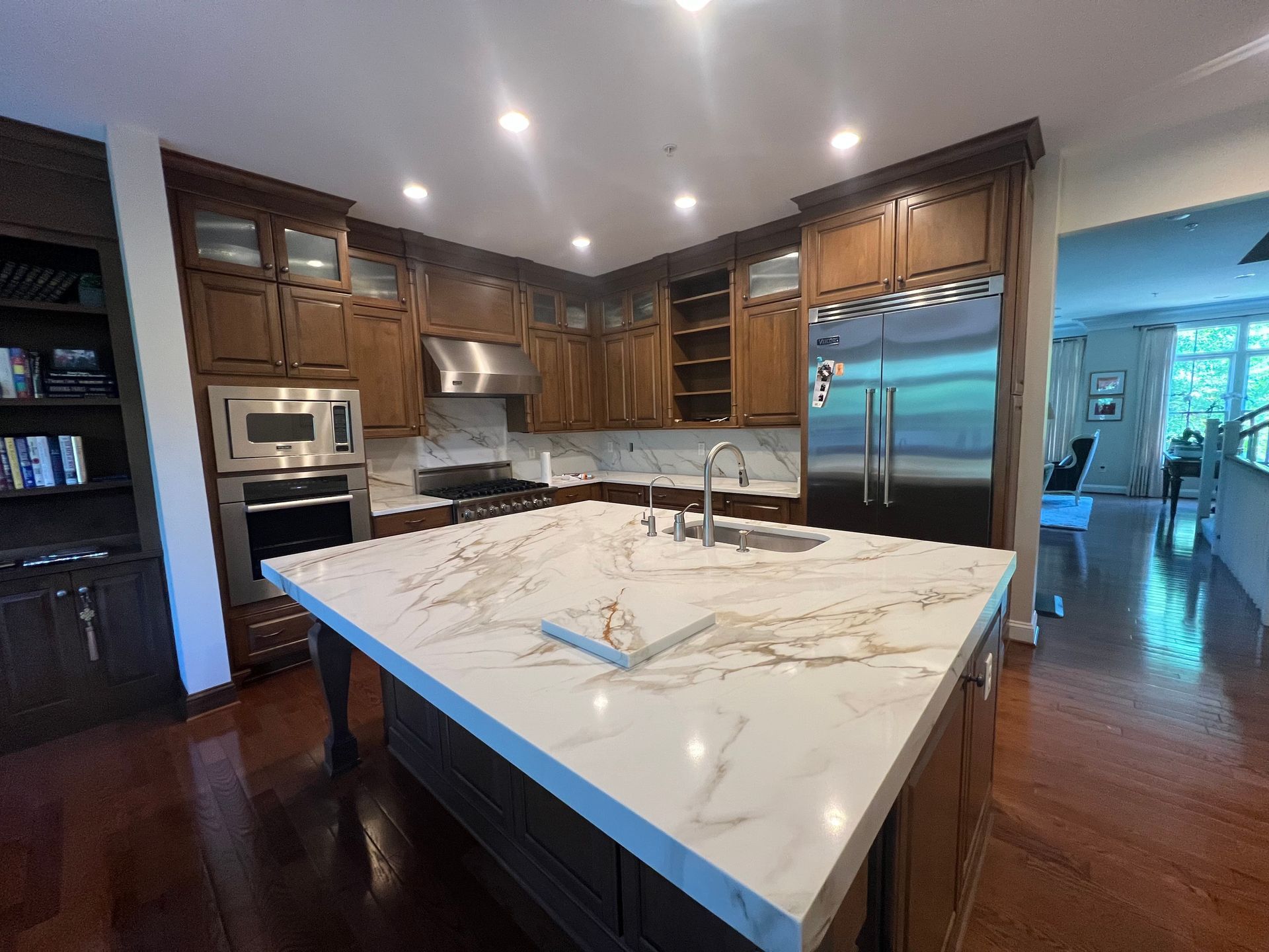 Modern kitchen with dark wood cabinets, large white island, stainless appliances, and hardwood floors