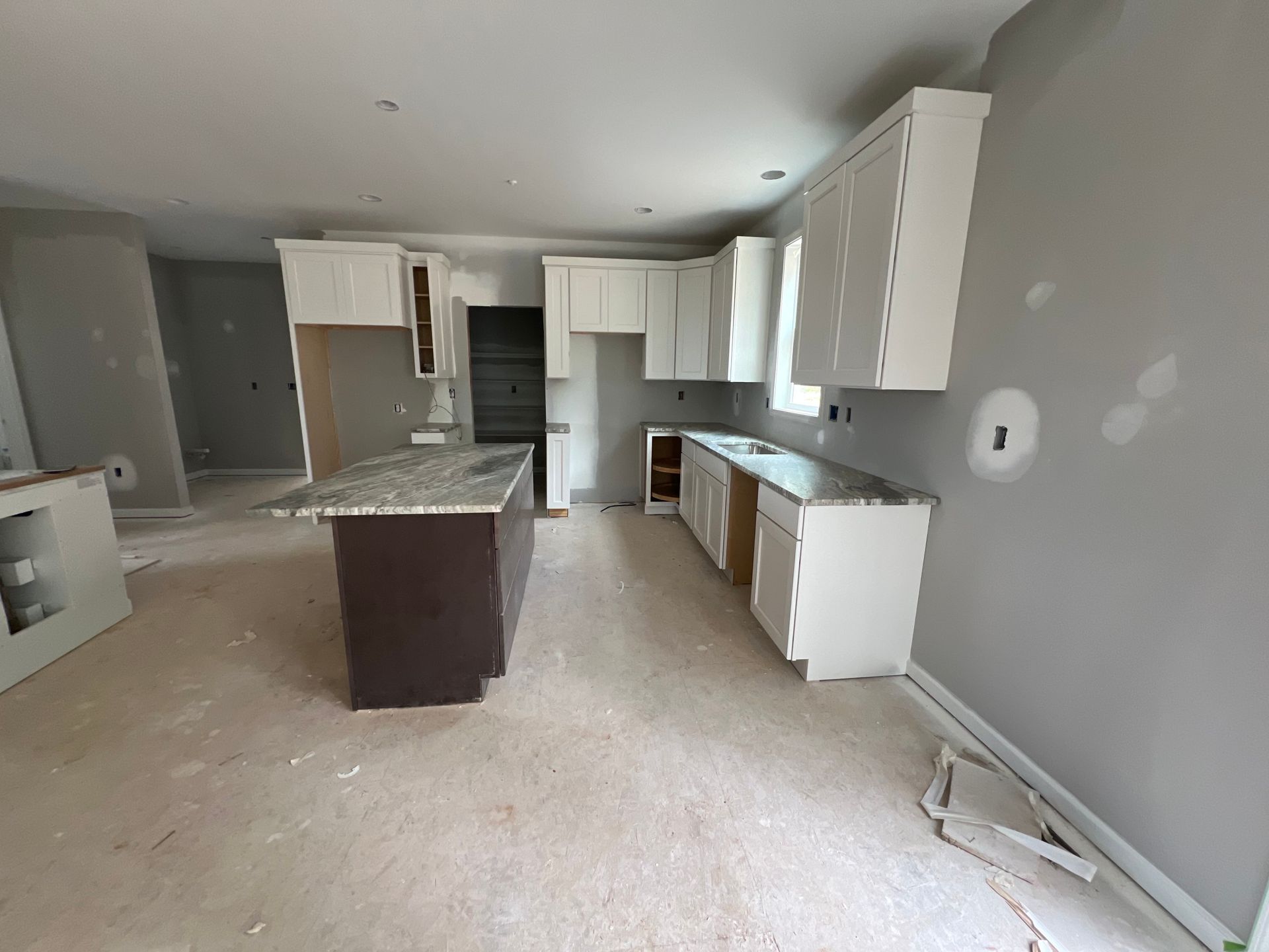 Empty kitchen with white cabinets, gray walls, and a dark island in an unfinished room.