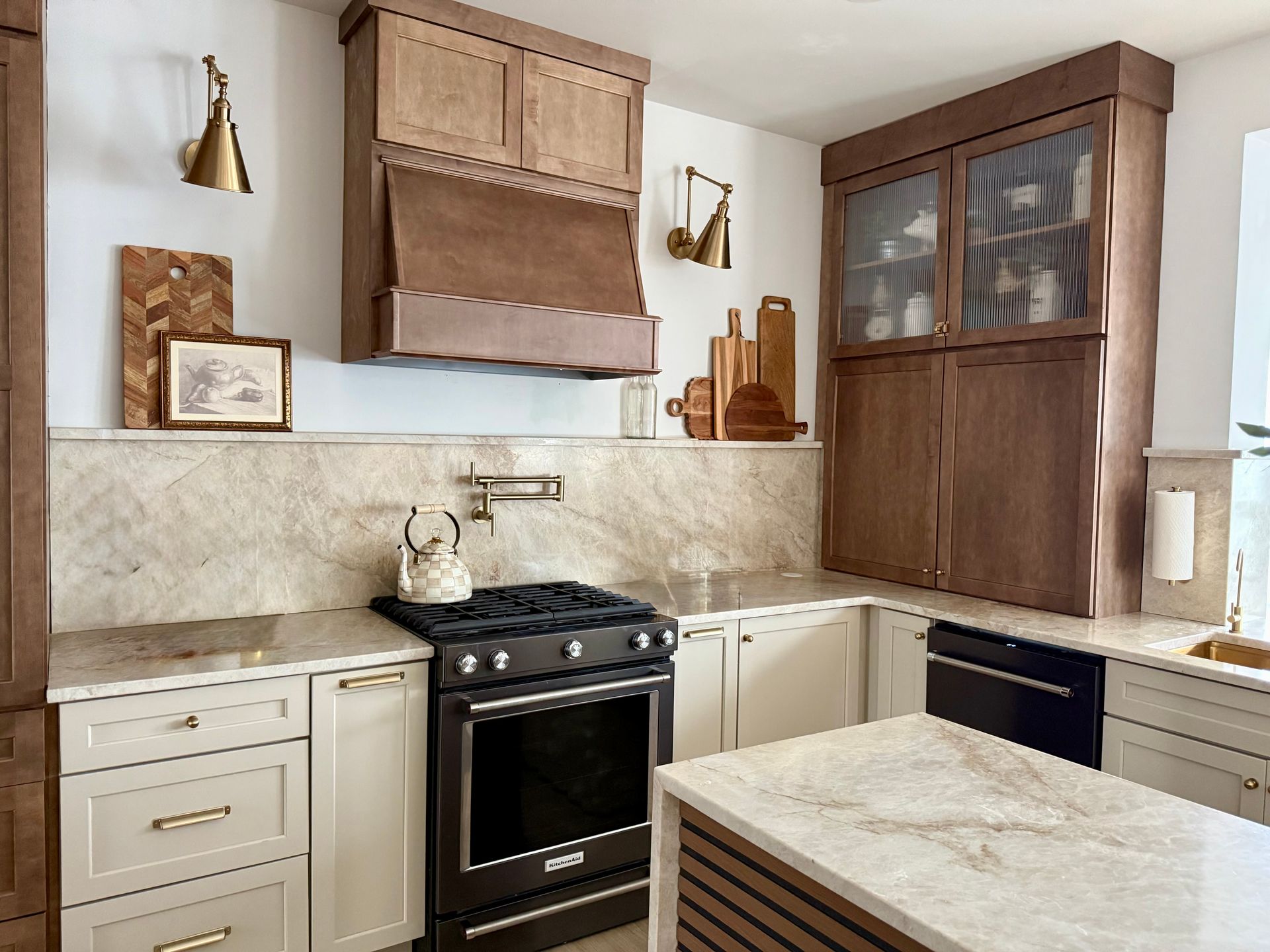 A beige kitchen with a gas stove, marble counters, and white cabinets beneath wooden wall units.